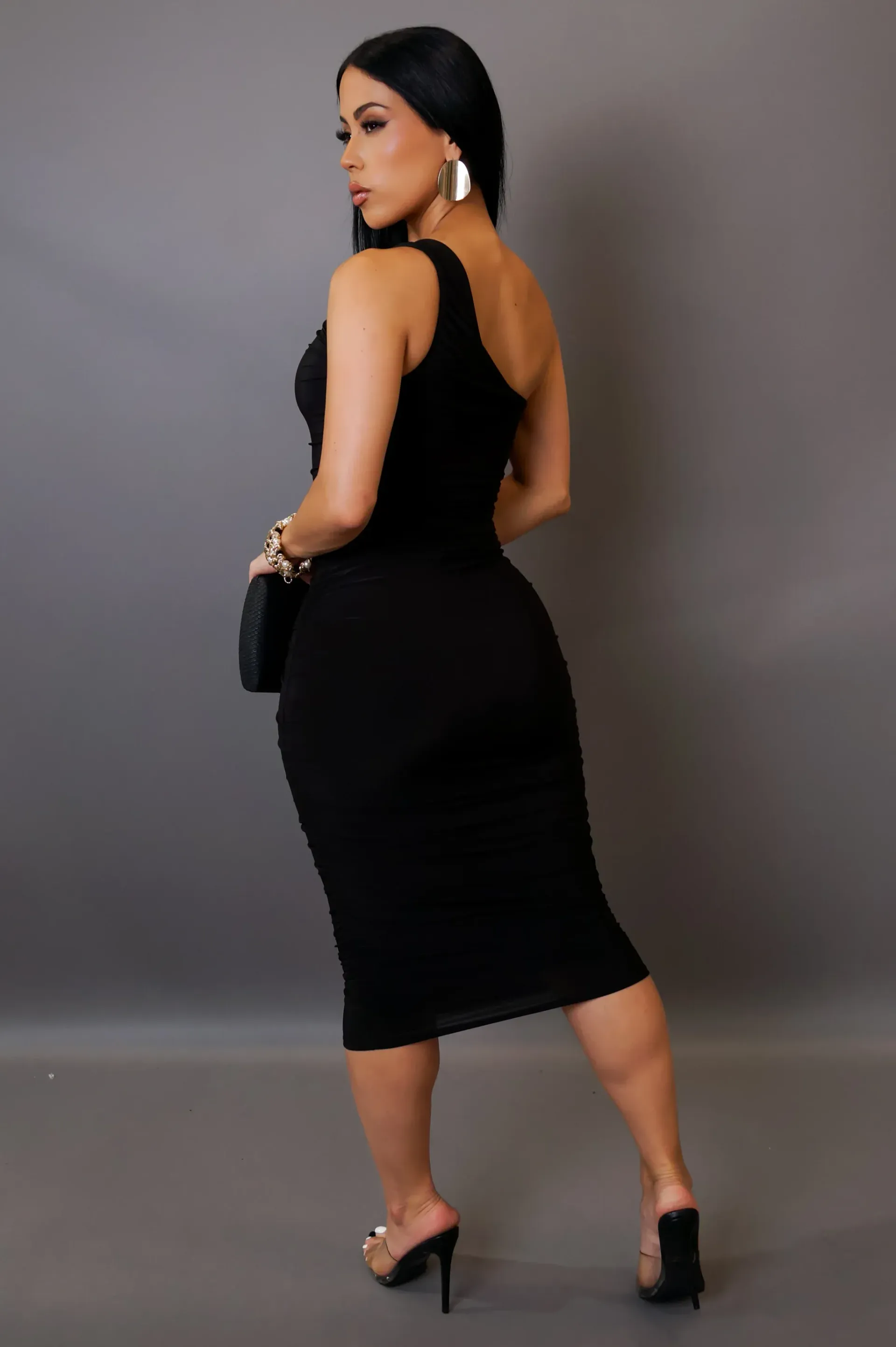 A woman is wearing a black one shoulder dress and holding a black clutch.