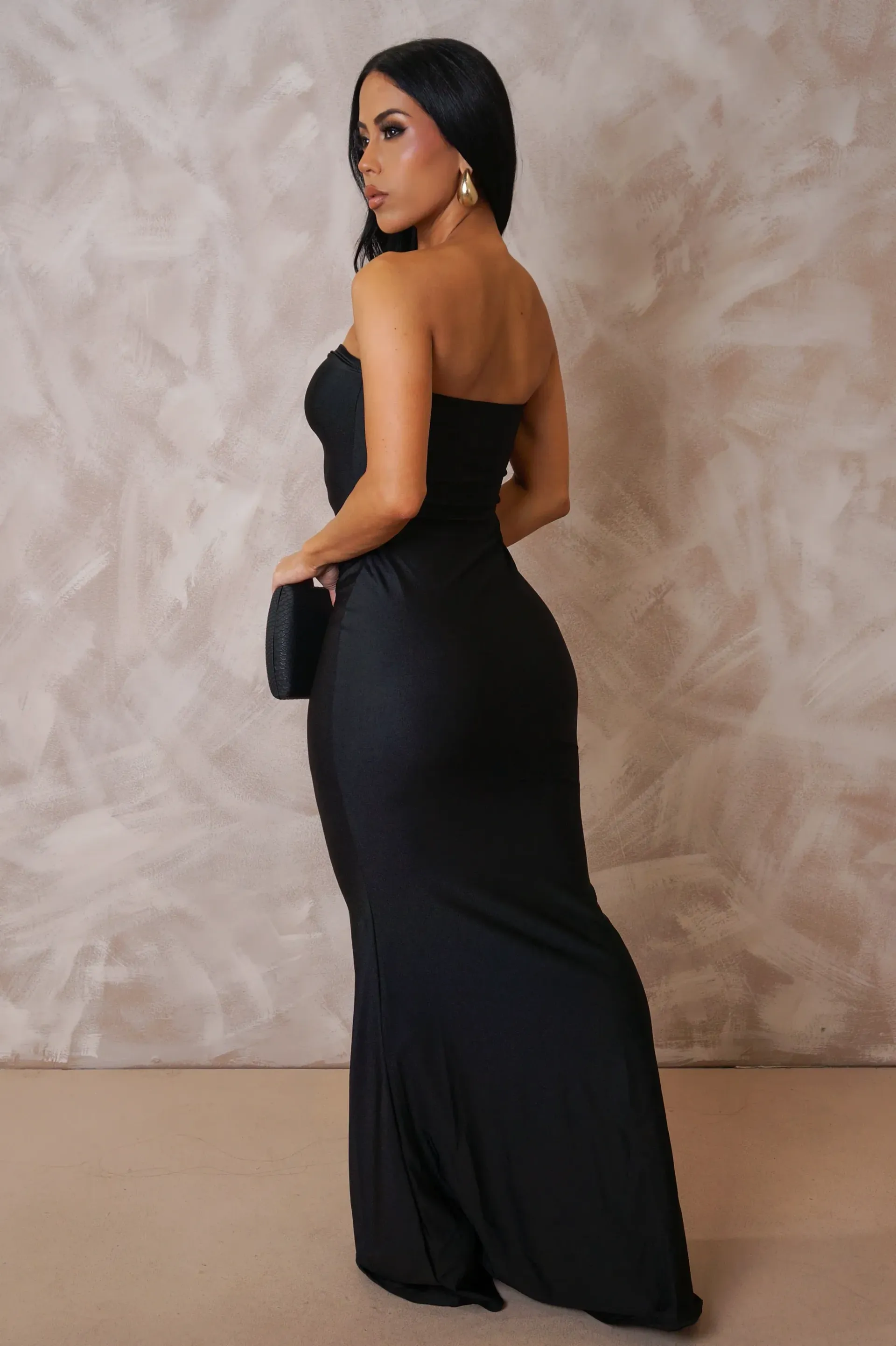 A woman is wearing a black dress and holding a black clutch.