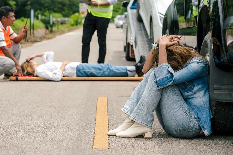 A woman is sitting on the ground next to a car after a car accident.