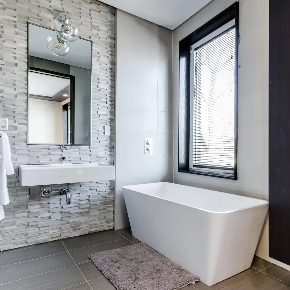 Modern bathroom with a white tub, sink, and mirror; gray tile floor and walls.