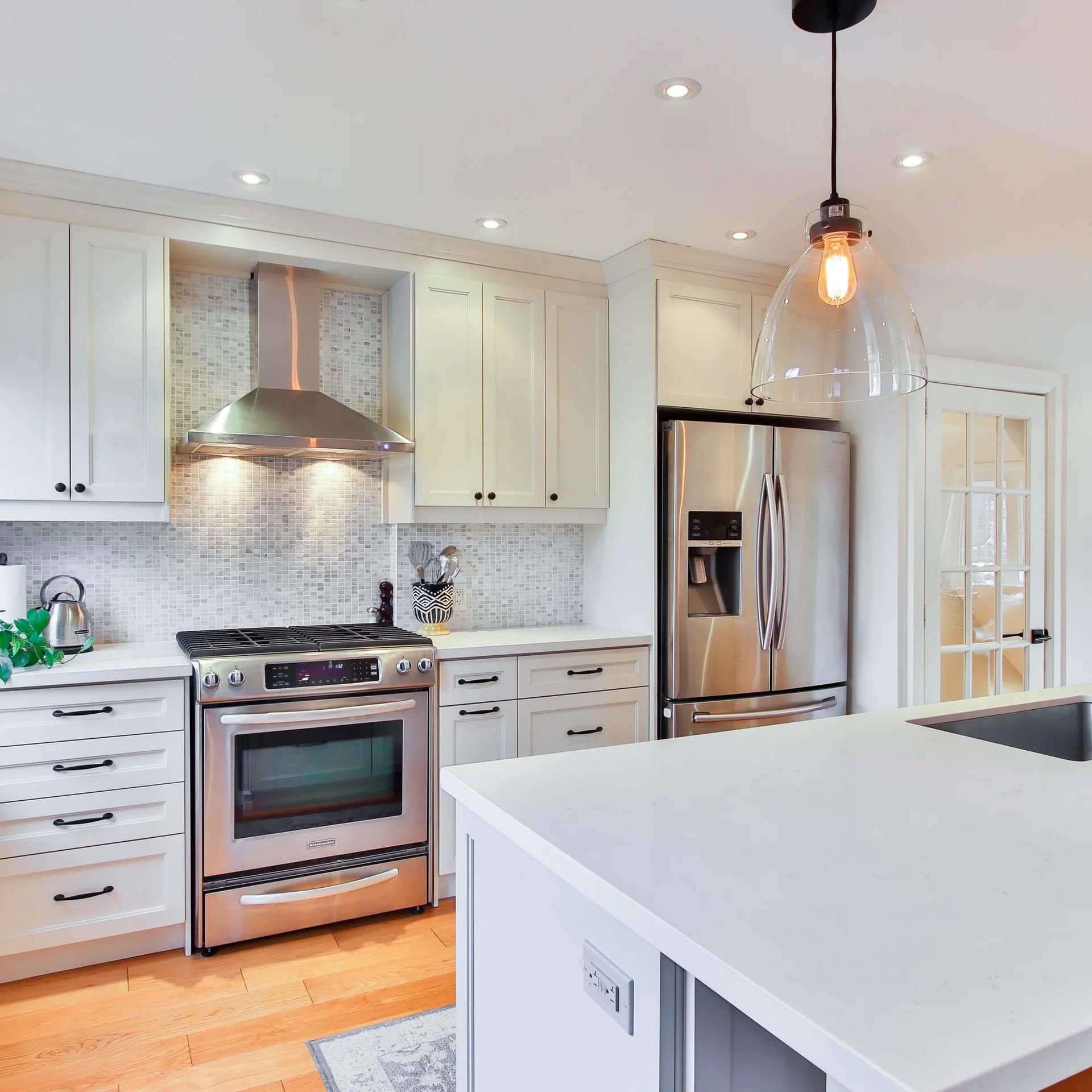 Modern white kitchen with stainless steel appliances, an island, and wood floors.