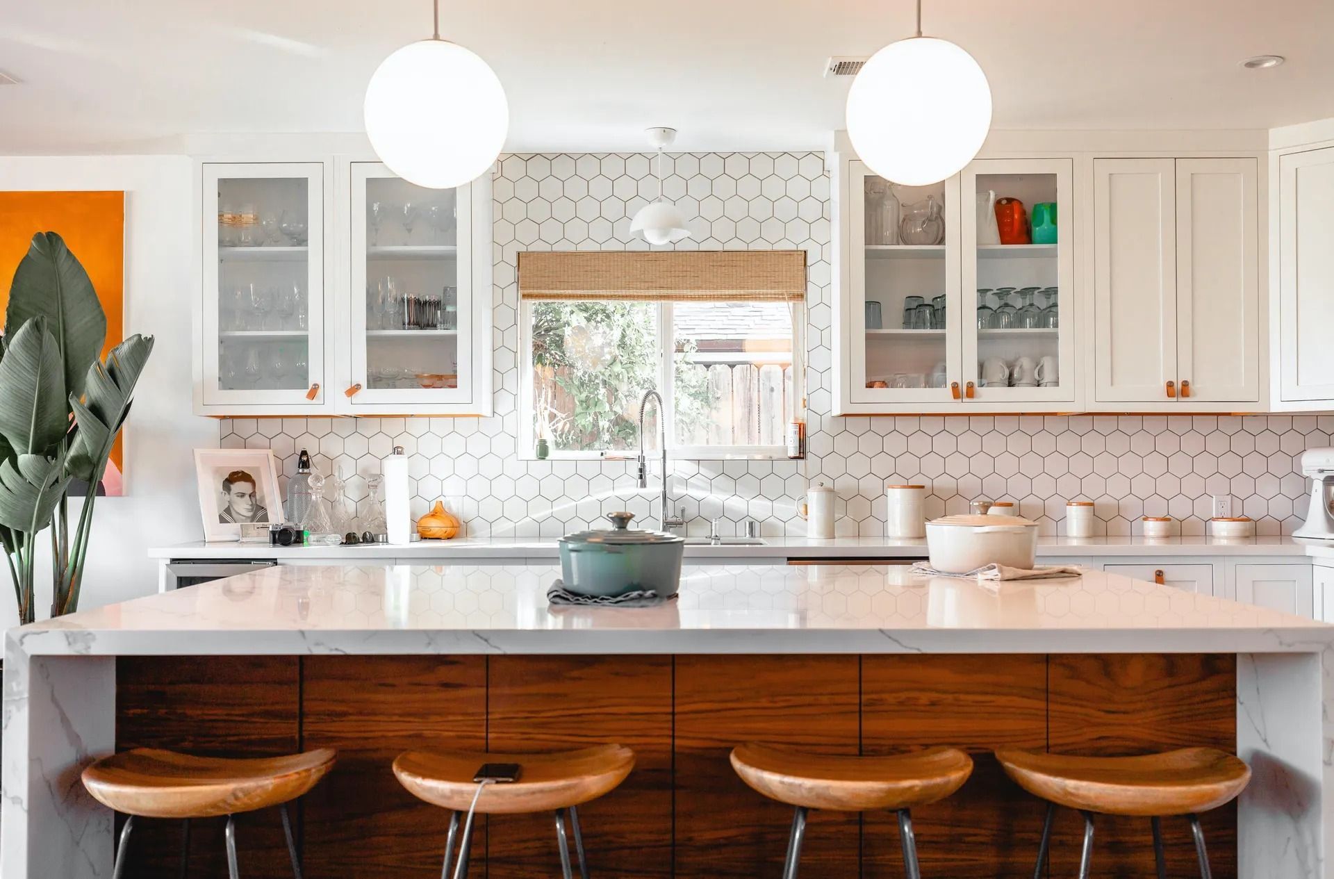 Modern white kitchen with island, wooden stools, overhead lights, and cabinets.