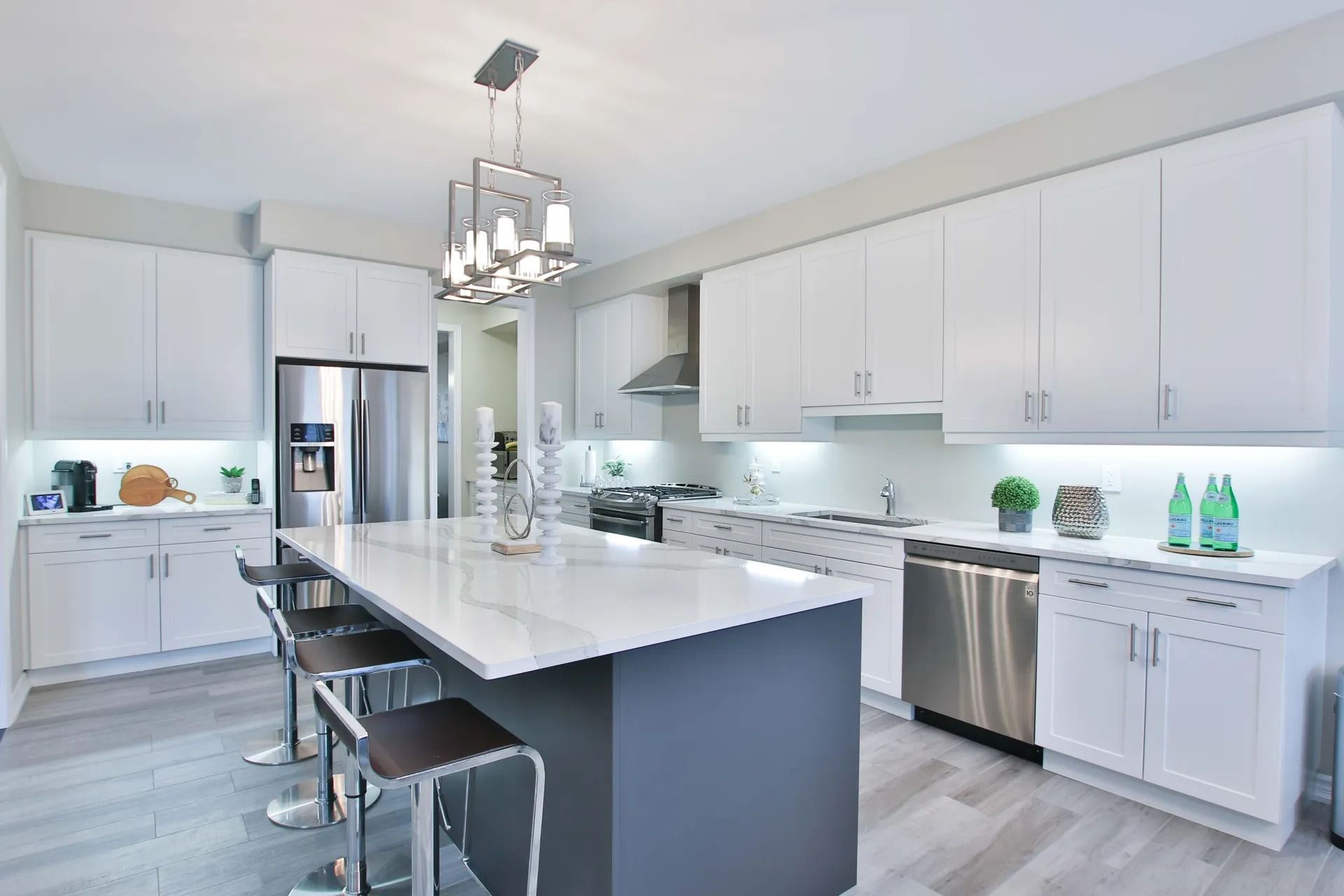 Modern white kitchen with a large island, stainless steel appliances, and gray flooring.