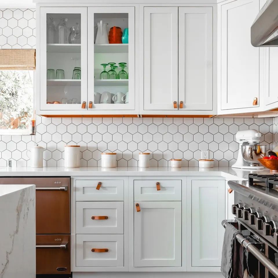 White kitchen with hexagonal backsplash, white cabinets, and copper-colored hardware and appliances.