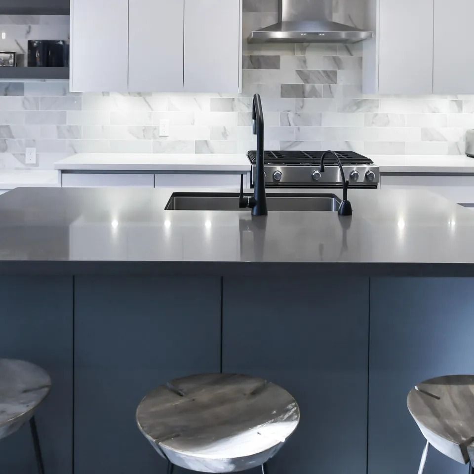 Modern kitchen with gray island, gas stovetop, black faucet, white cabinets, and silver stools.