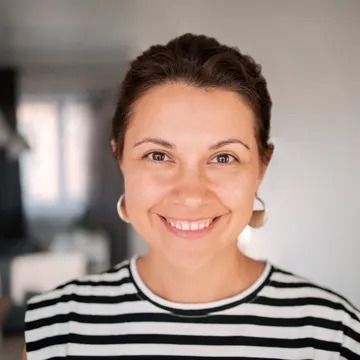 Woman with brown hair smiling, wearing a black and white striped shirt and gold hoop earrings.
