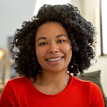 Woman with curly dark hair smiles, wearing a red shirt.