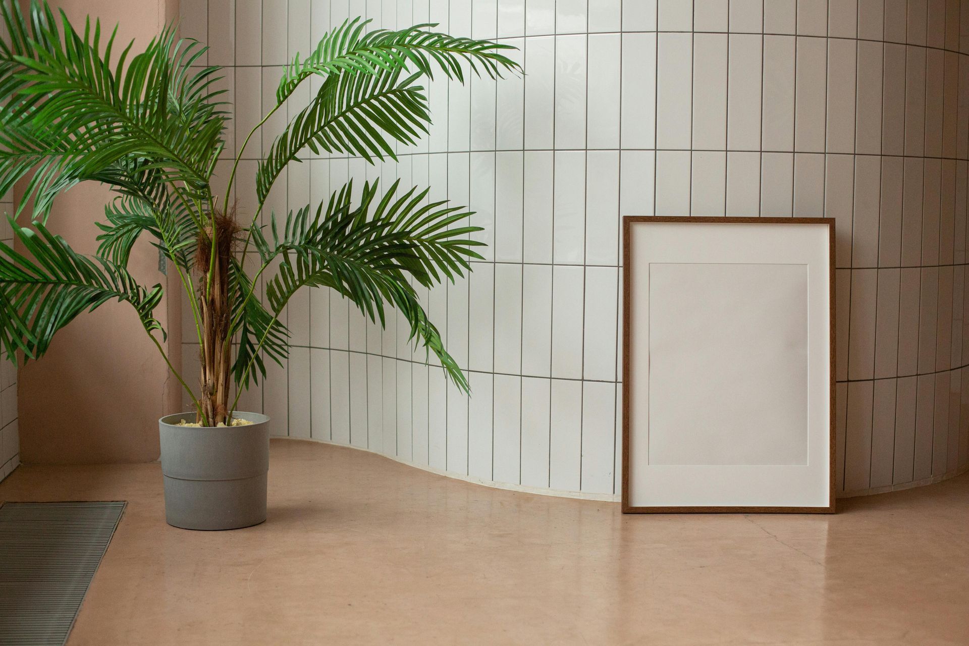 Palm in pot, framed blank print against curved, textured wall and rose-colored floor.