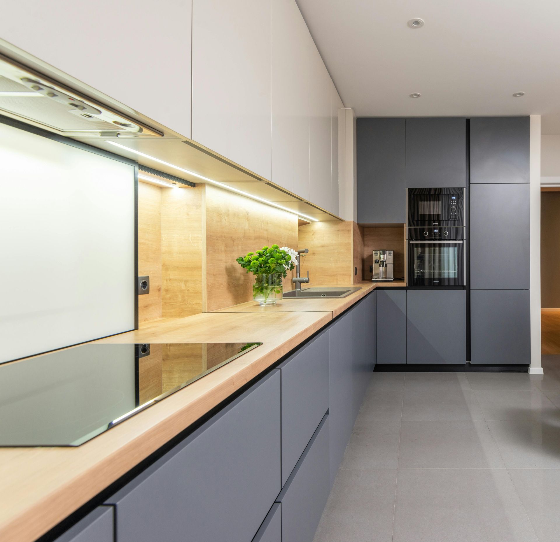 Modern gray and wood-toned kitchen with built-in appliances and sleek cabinetry; countertop lighting.
