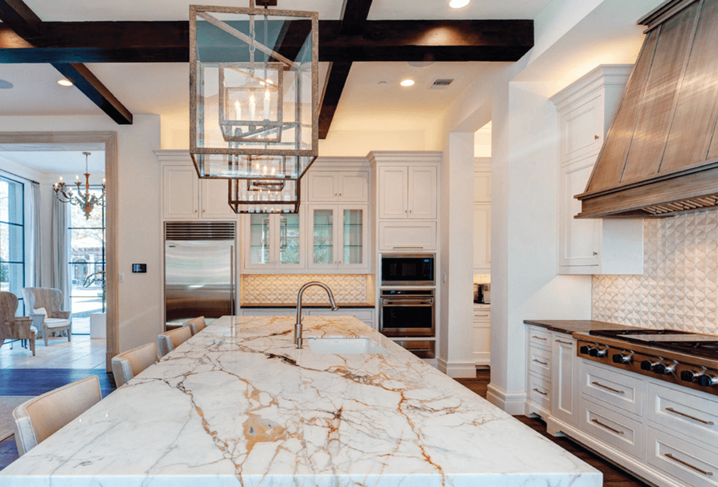 Luxury white kitchen with marble island, stainless steel appliances, and dark wooden beams.