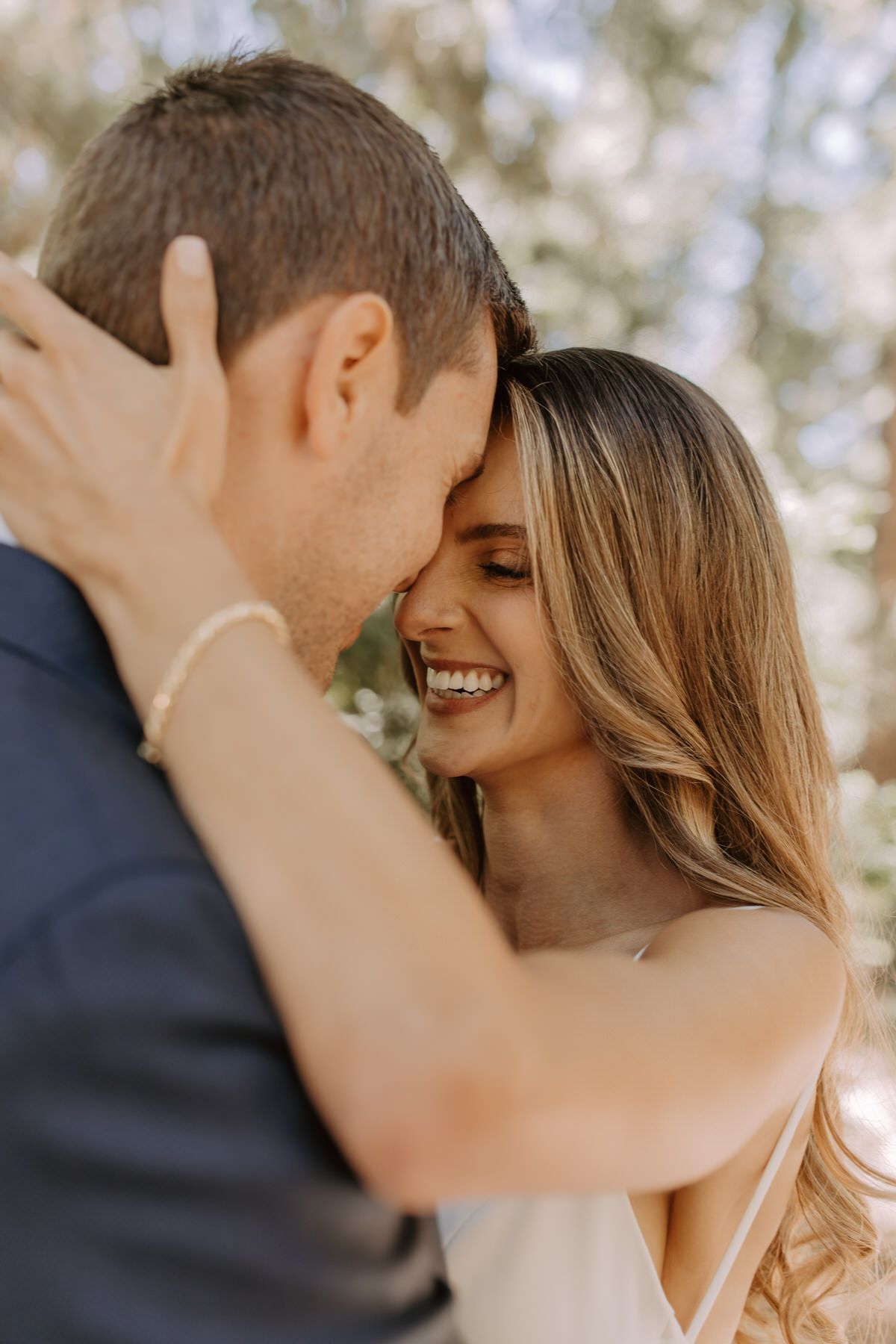 A bride and groom are hugging each other and smiling featuring her flawless makeup.