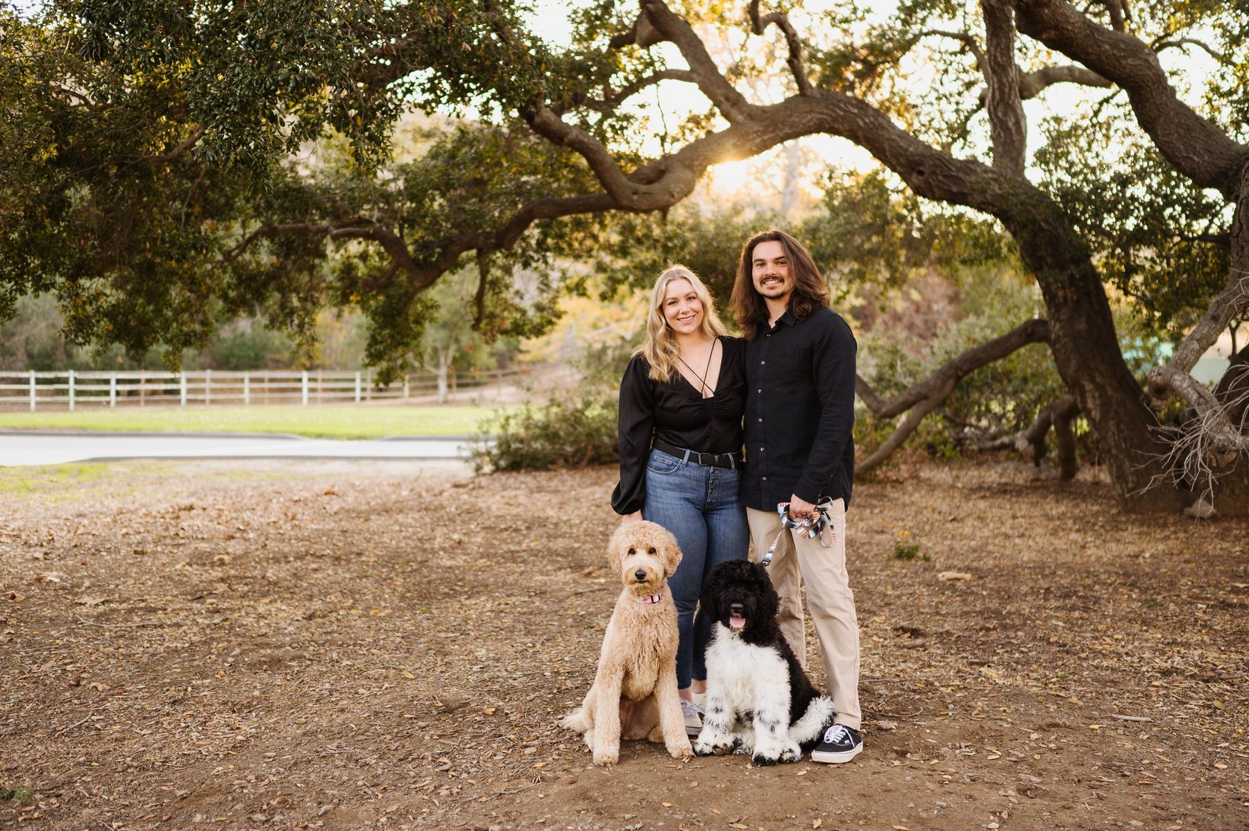 A man and a woman are posing for a picture with their dogs in a park. Orange county hair and makeup artist.