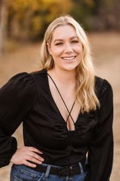 A woman in a black top and jeans is smiling for the camera. Orange county hair and makeup artist.