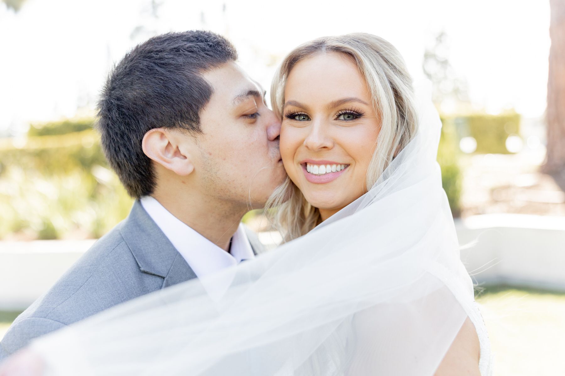A bride and groom are kissing under their veil with beautiful makeup.