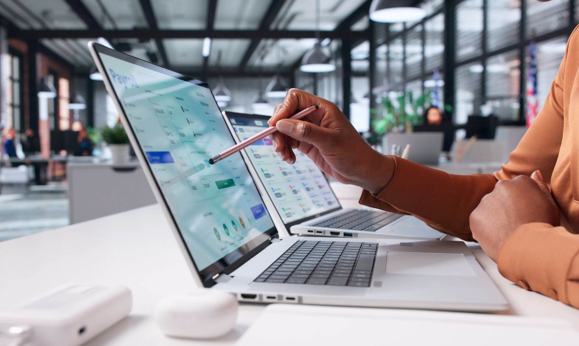 Person using a laptop and pointing at a spreadsheet on a desk in an office setting