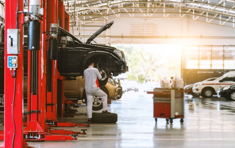 Car Lift in Auto Repair Shop With Mechanic Working on a Black Car — Precision Tuning in Trinity Beach, QLD