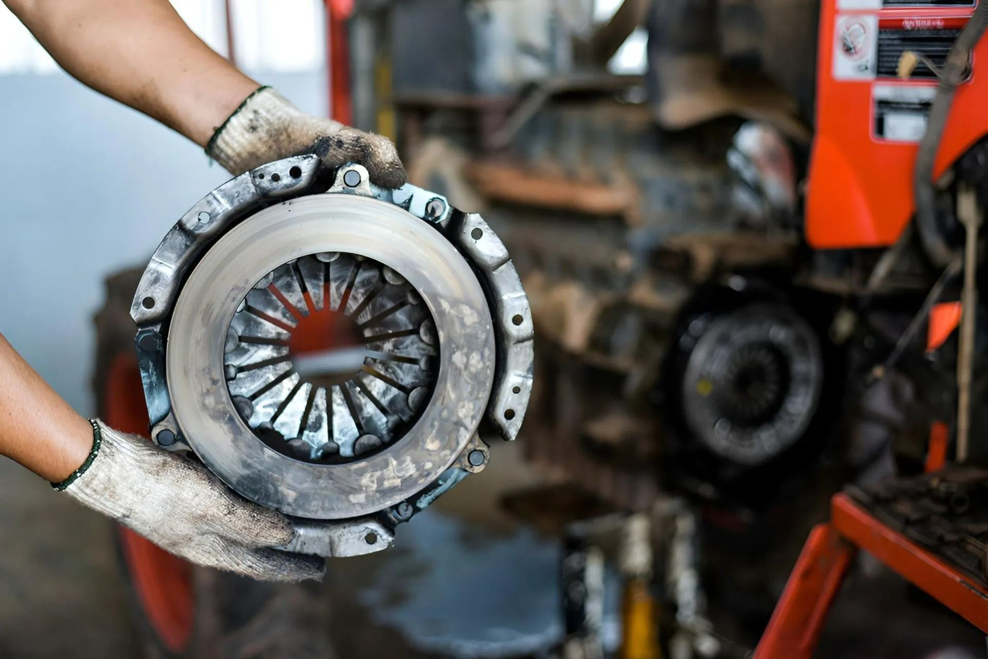 Hands in Gloves Holding a Car Clutch Assembly, with Orange Machinery — Precision Tuning in Bungalow, QLD