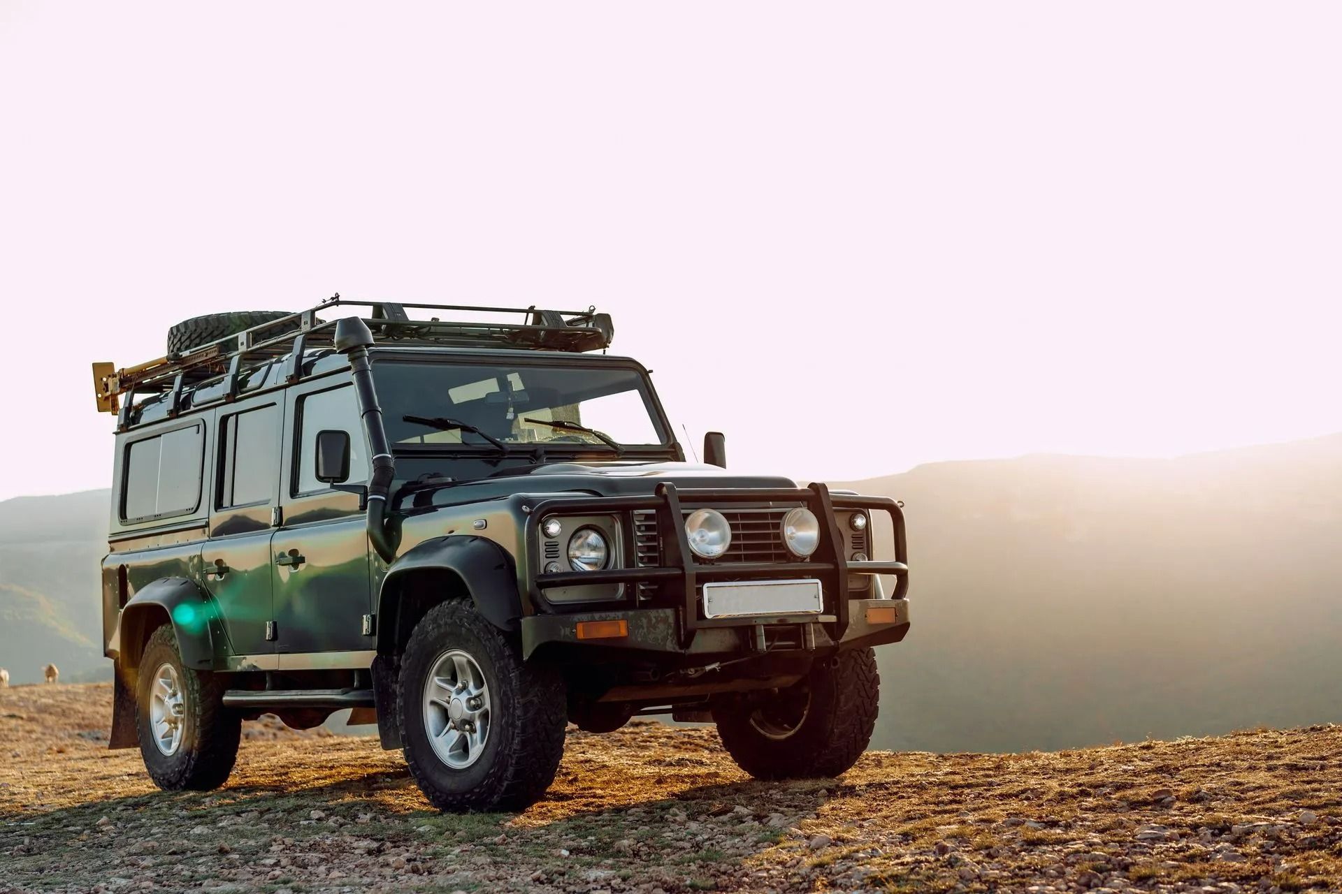 Dark Green Land Rover Defender Parked on A Rocky Hilltop, with Gear on Roof Rack — Precision Tuning in Bungalow, QLD