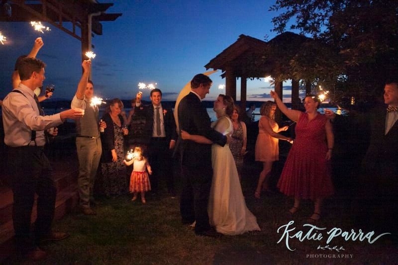 A bride and groom are kissing while their guests hold sparklers