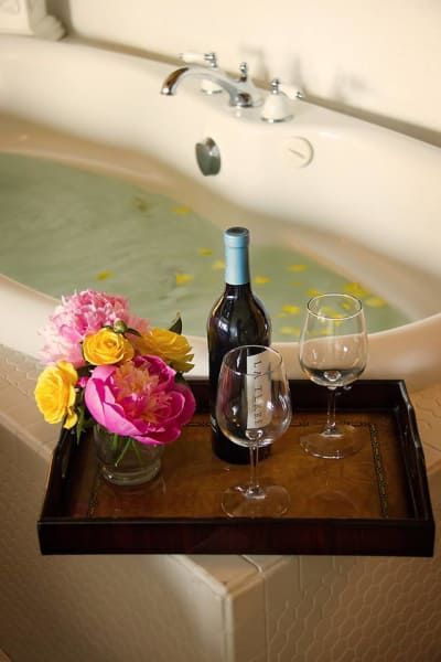 A tray with a bottle of wine and two glasses sits next to a bathtub