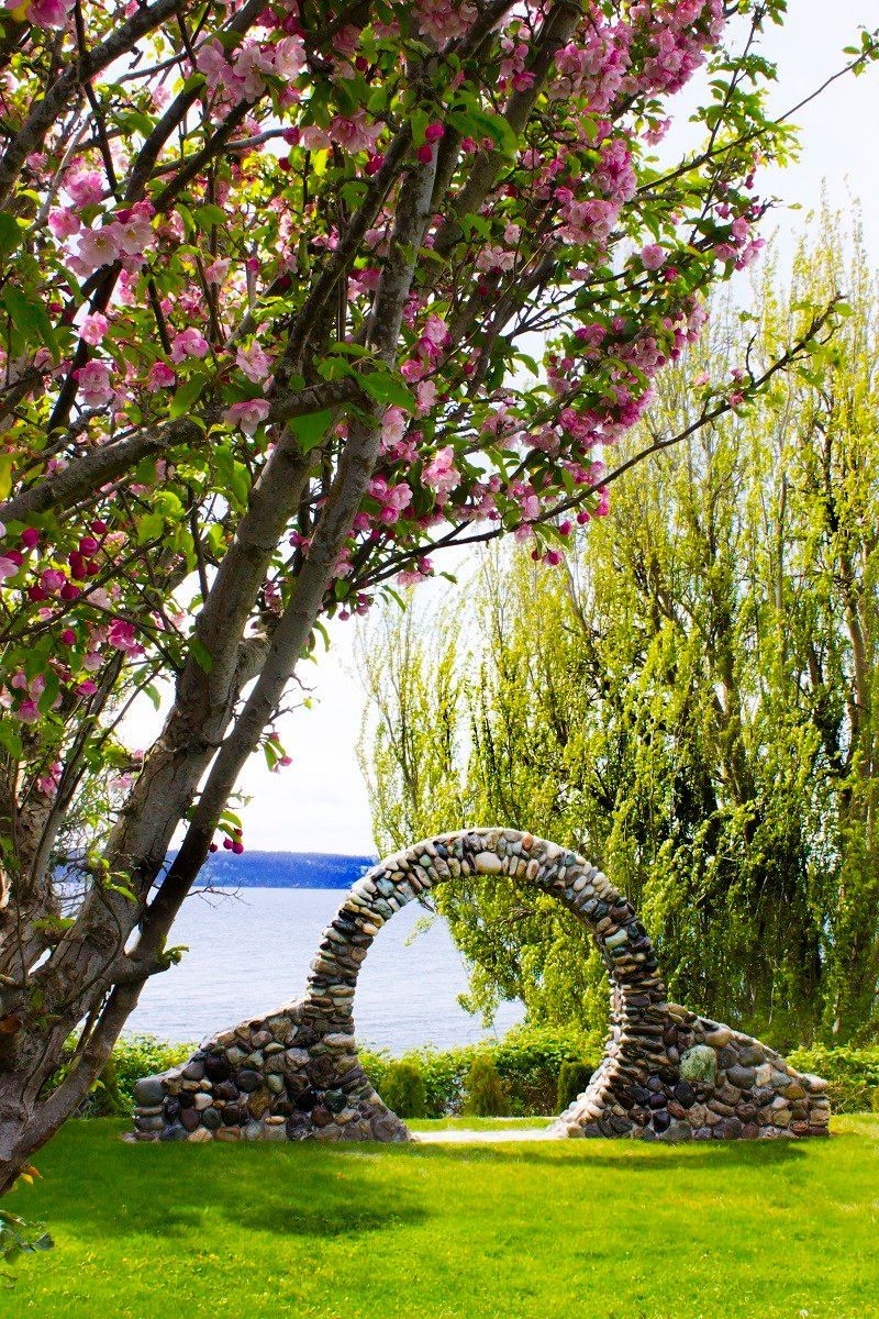 A stone archway in the middle of a park next to a tree with pink flowers.