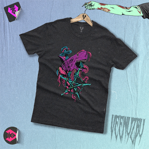 Camiseta preta com estampa gráfica colorida estendida sobre um fundo azul, com pequenos adesivos e um cabide por perto.