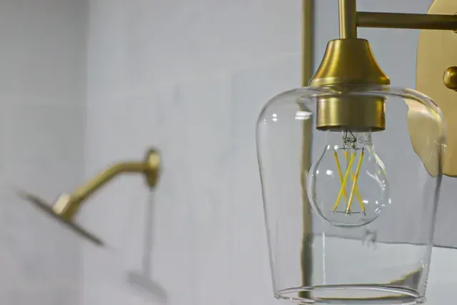 A close up of a light bulb hanging from a wall next to a shower head.