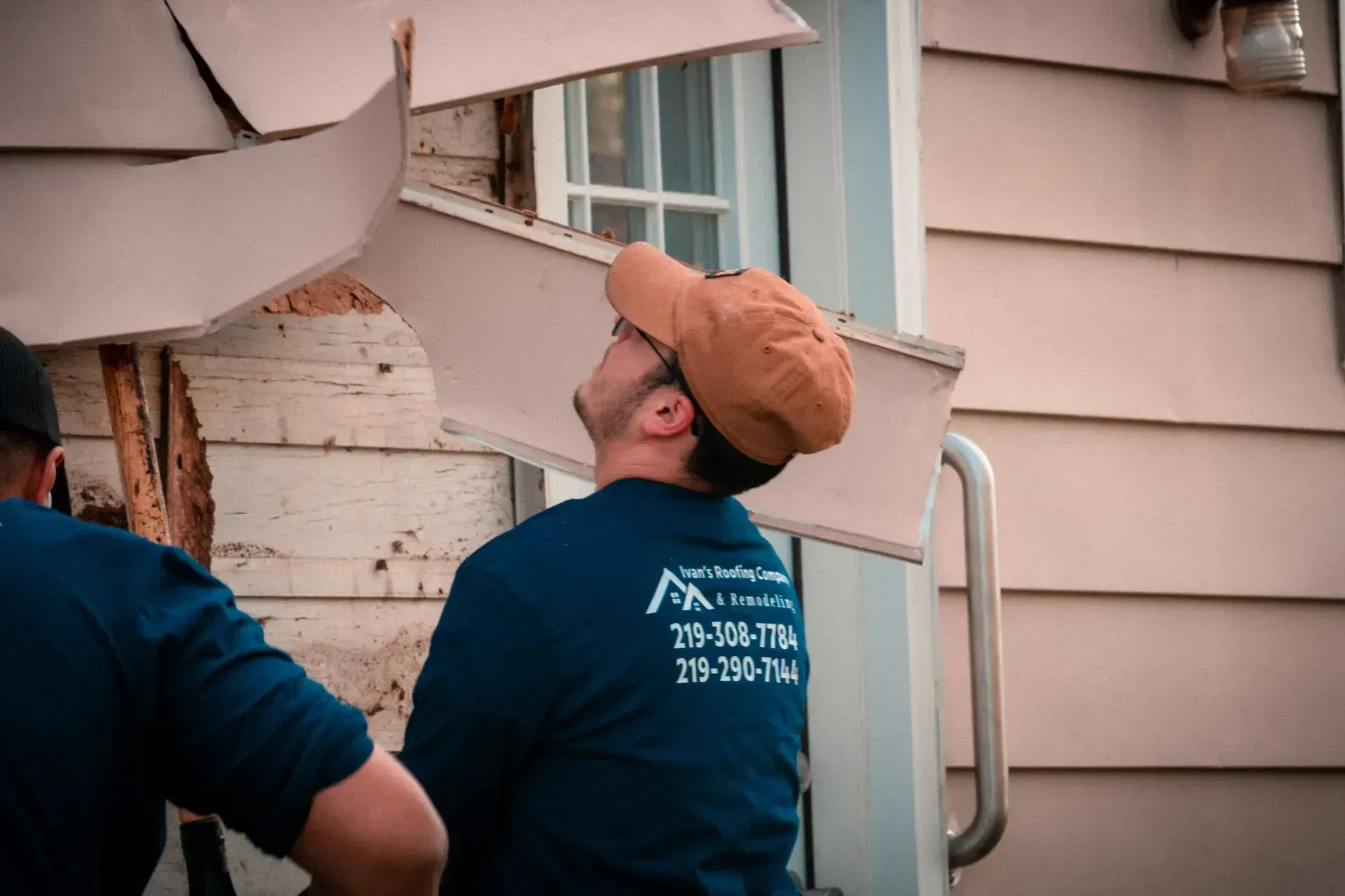 A man wearing a hat and glasses is standing in front of a house.