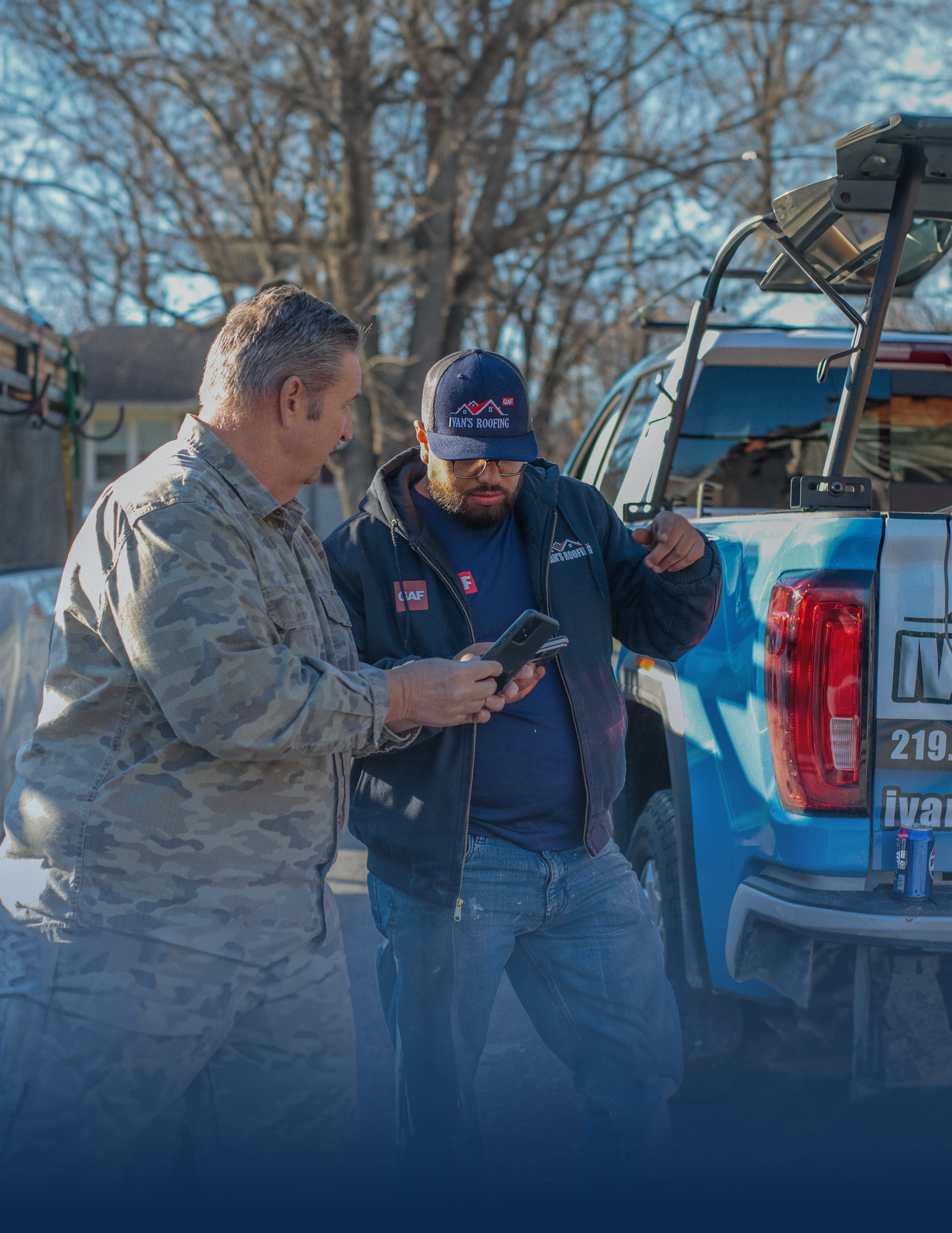 Two men are standing next to a truck looking at a tablet.