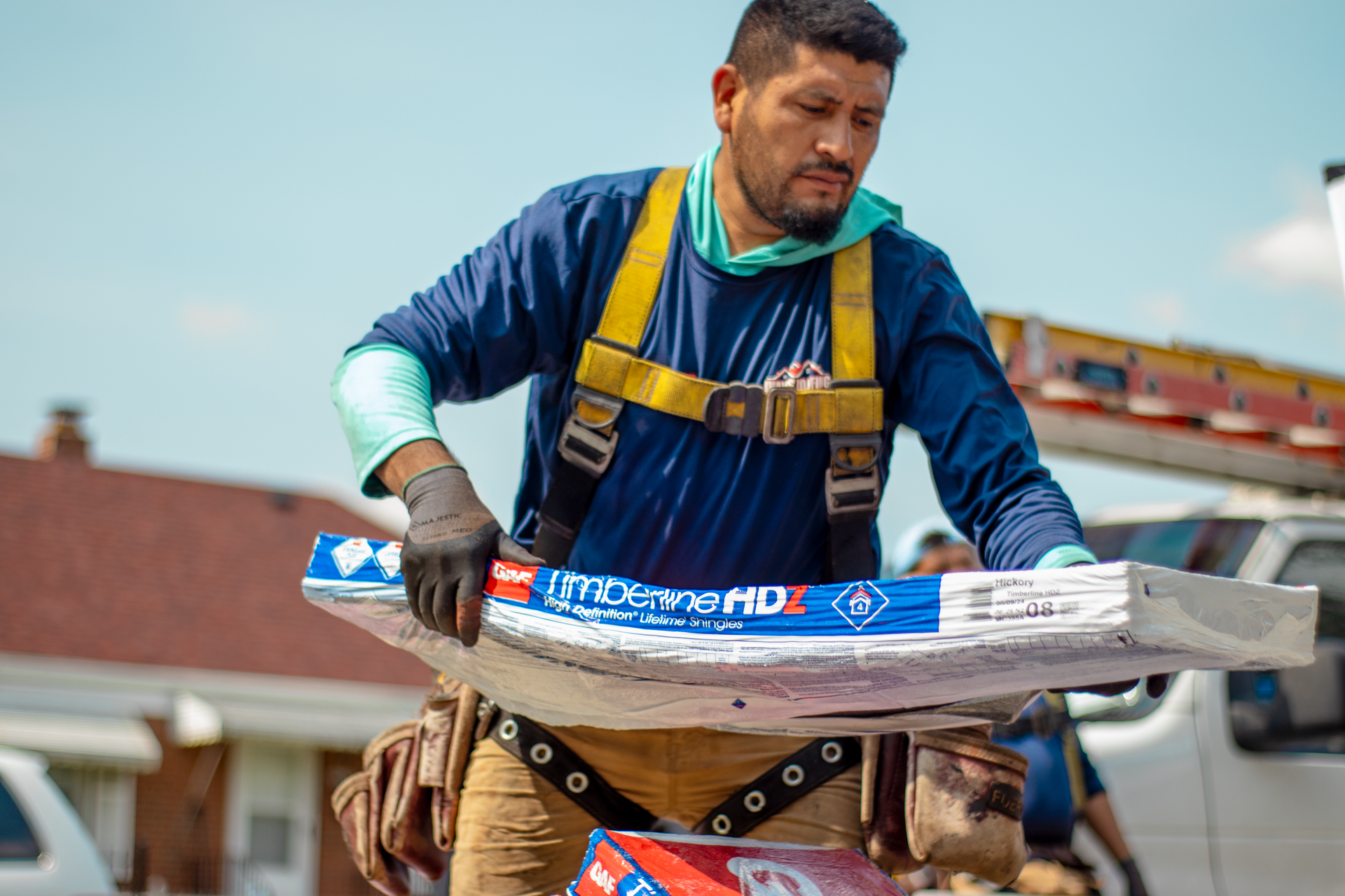 A man in a blue shirt and yellow harness is holding a piece of aluminum foil.