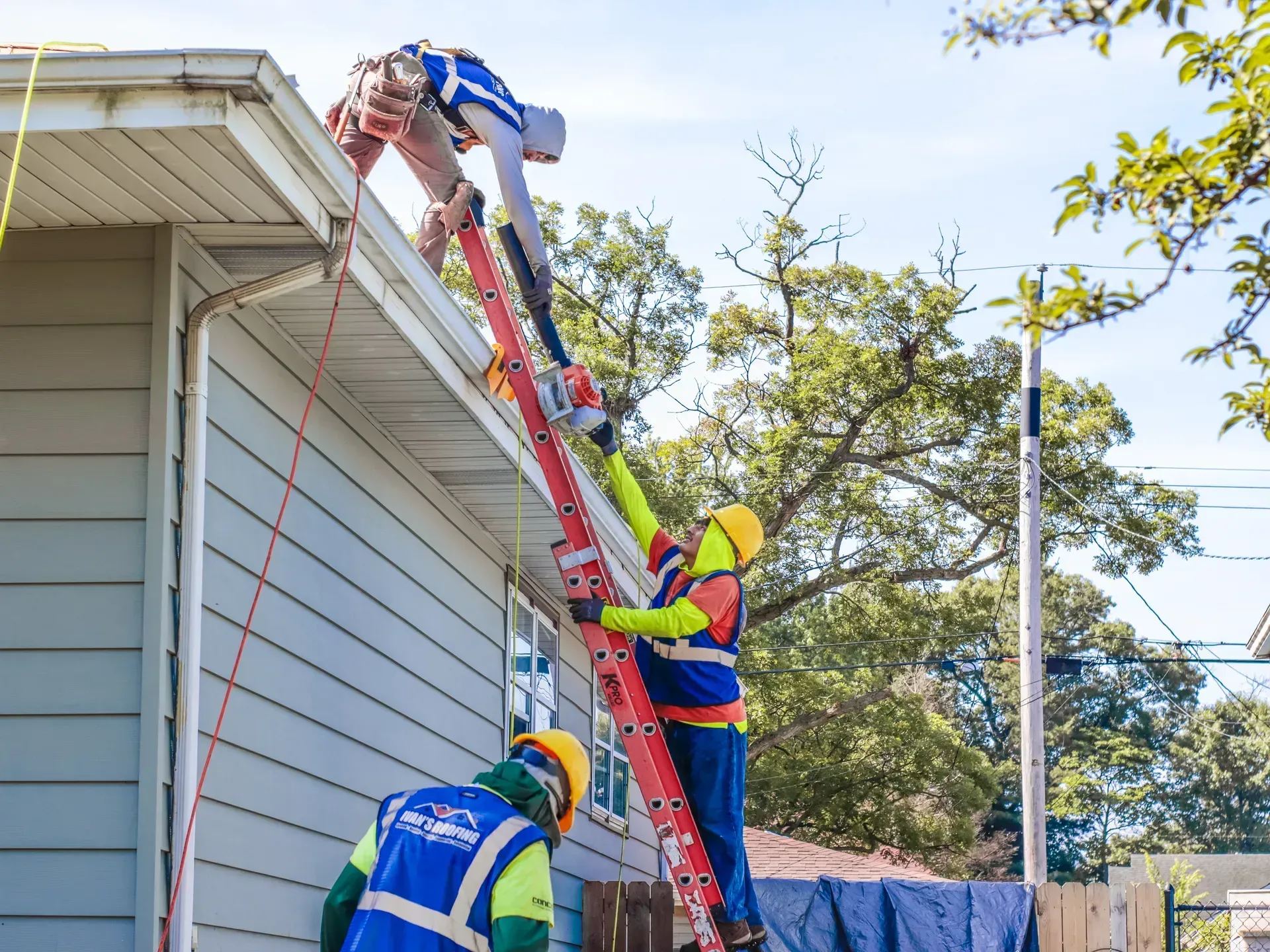 Two men are working on the roof of a house with ladders.