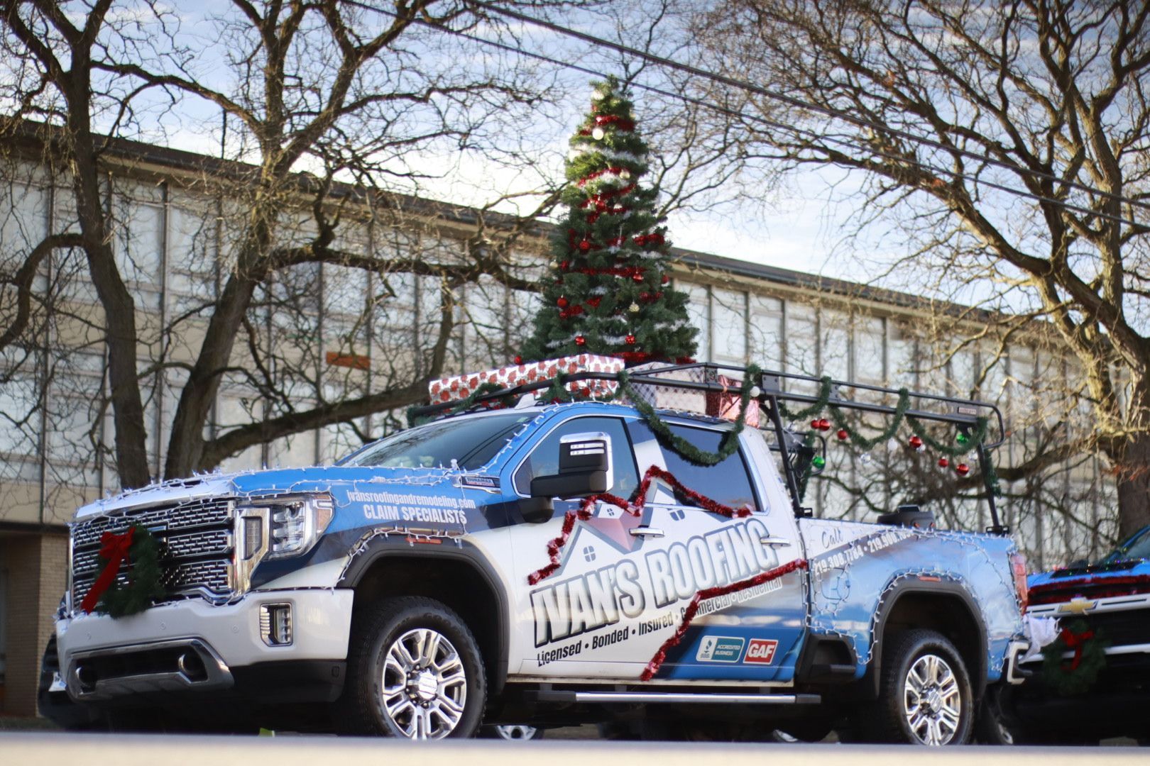 A truck with a christmas tree on top of it is parked in front of a building.