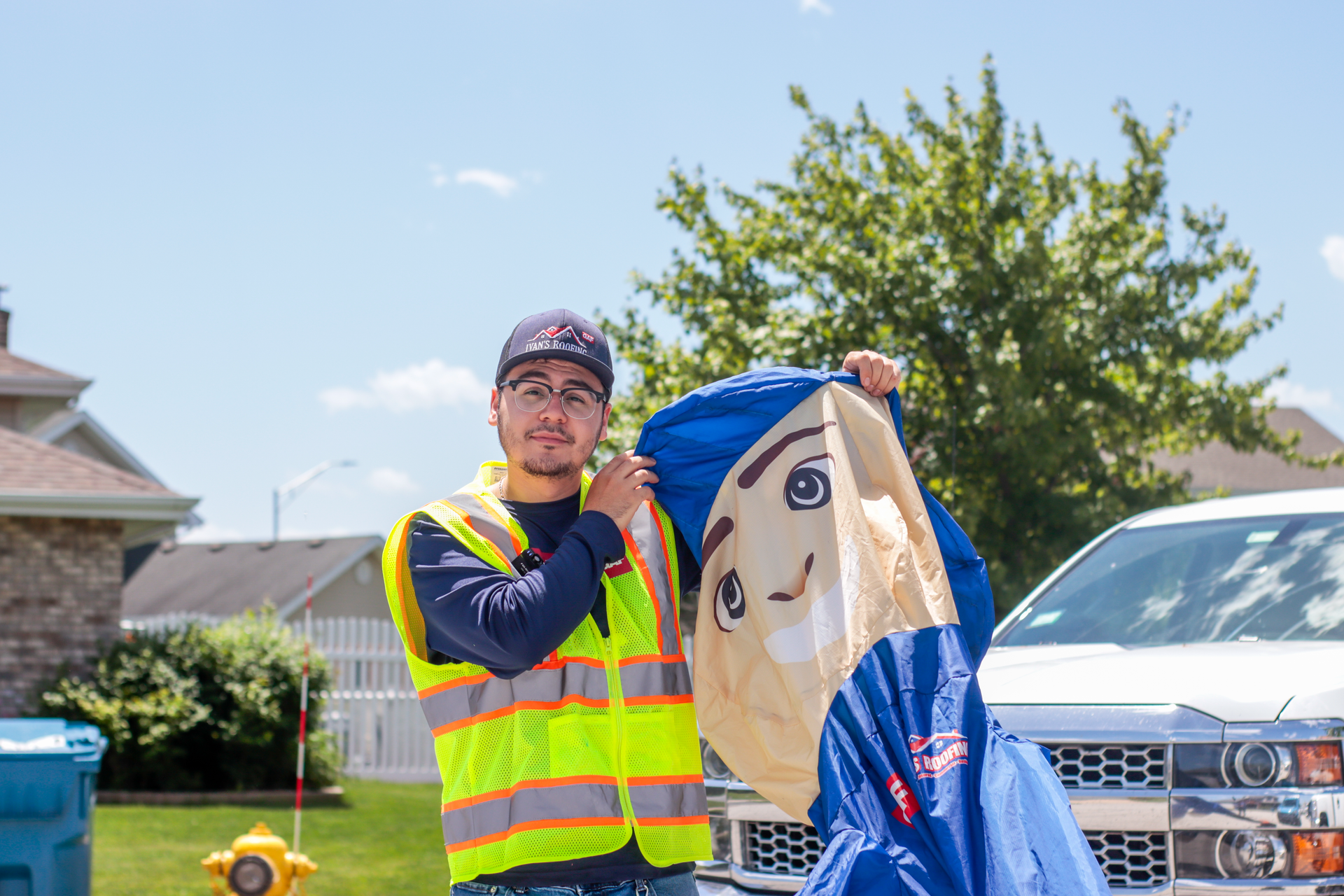 A man in a yellow vest is holding a scarecrow in front of a white truck.