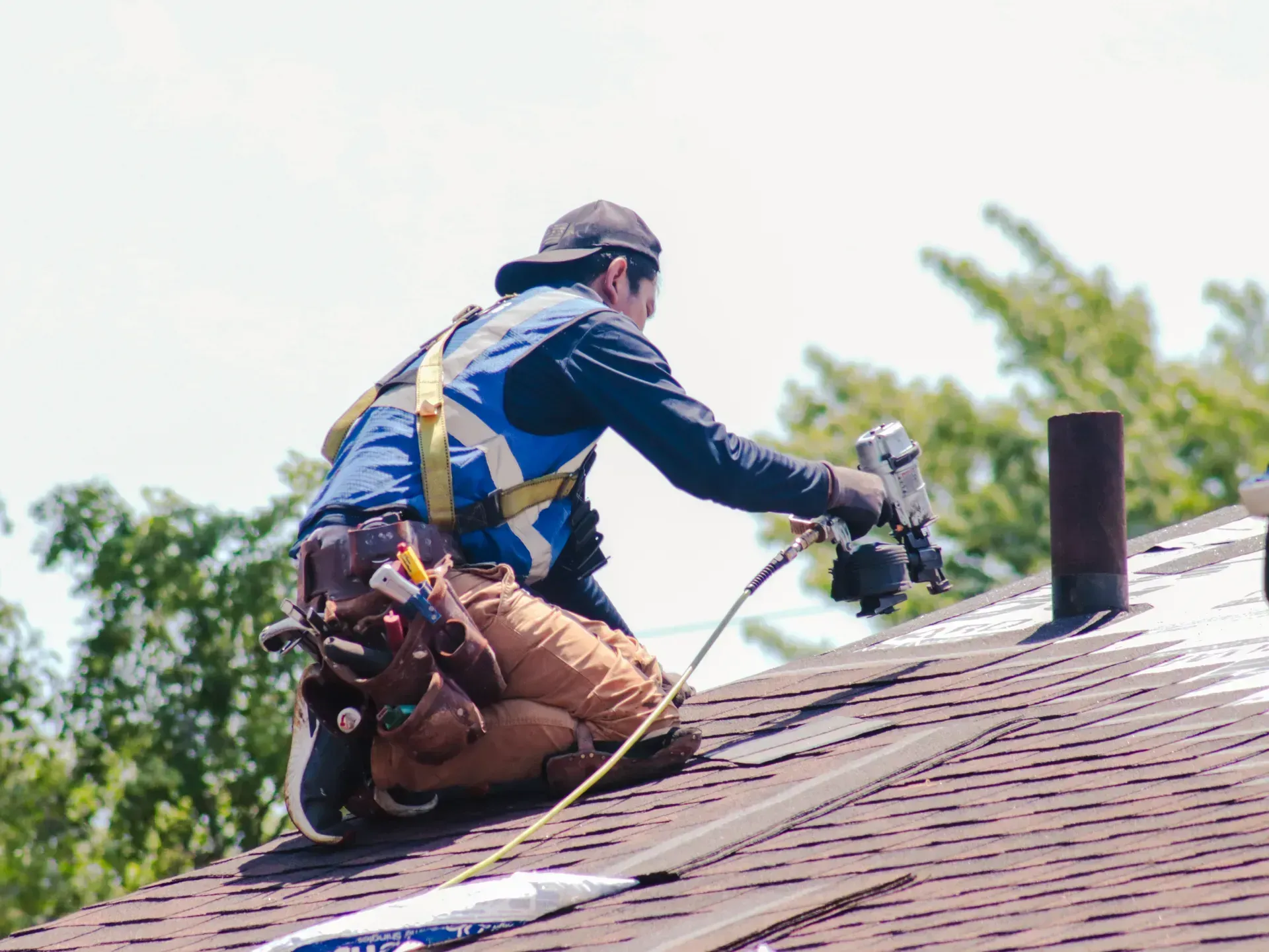 A man is kneeling on top of a roof working on it.