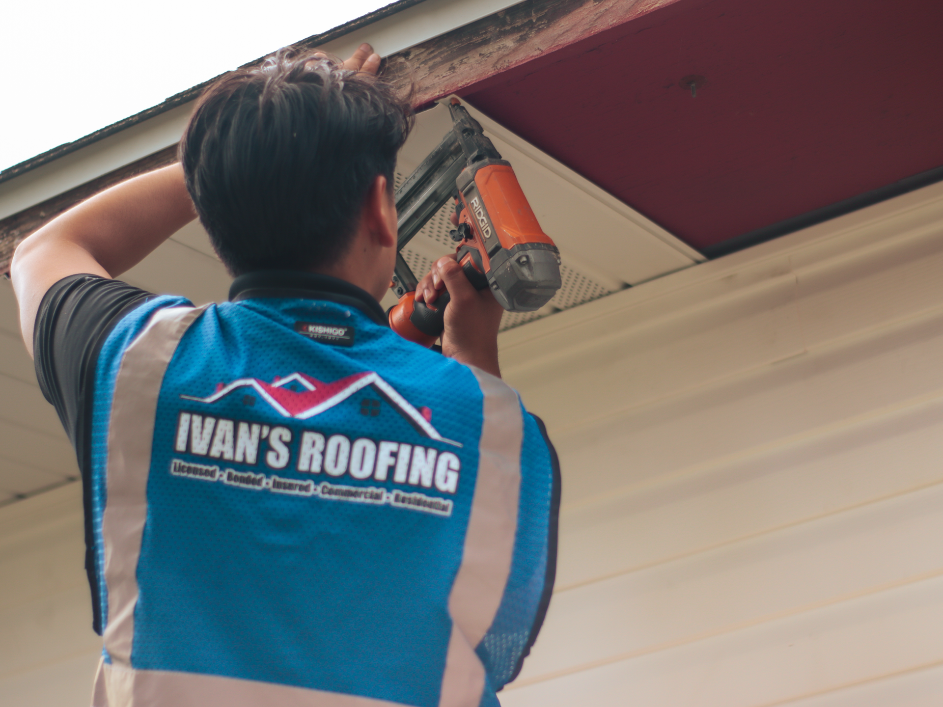A man wearing a blue vest that says ivan 's roofing is working on a roof