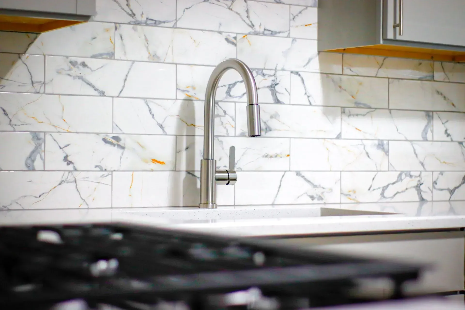 A kitchen with a sink, stove, and marble tiles on the wall.