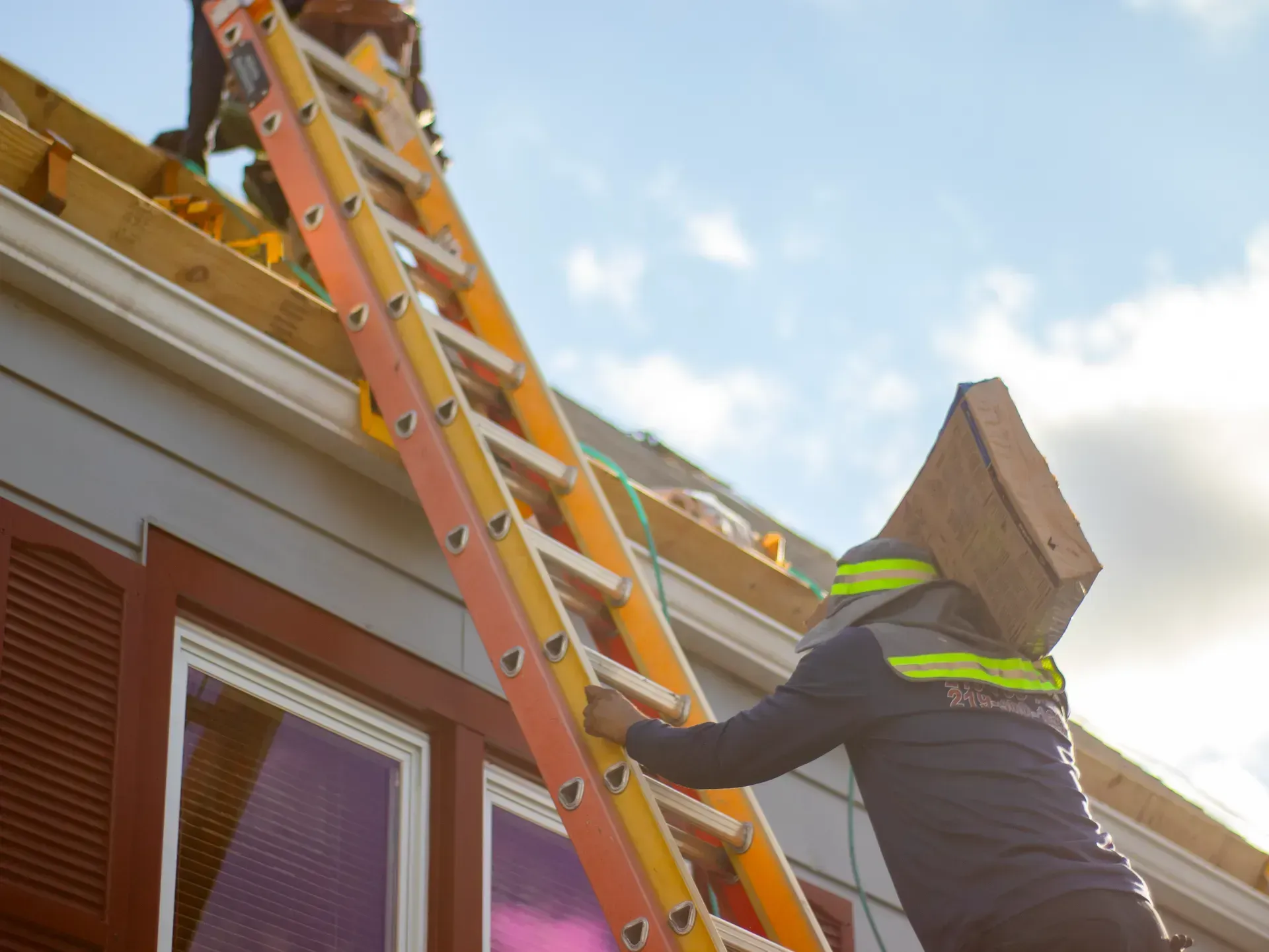 A man with a box on his head is climbing up a ladder.