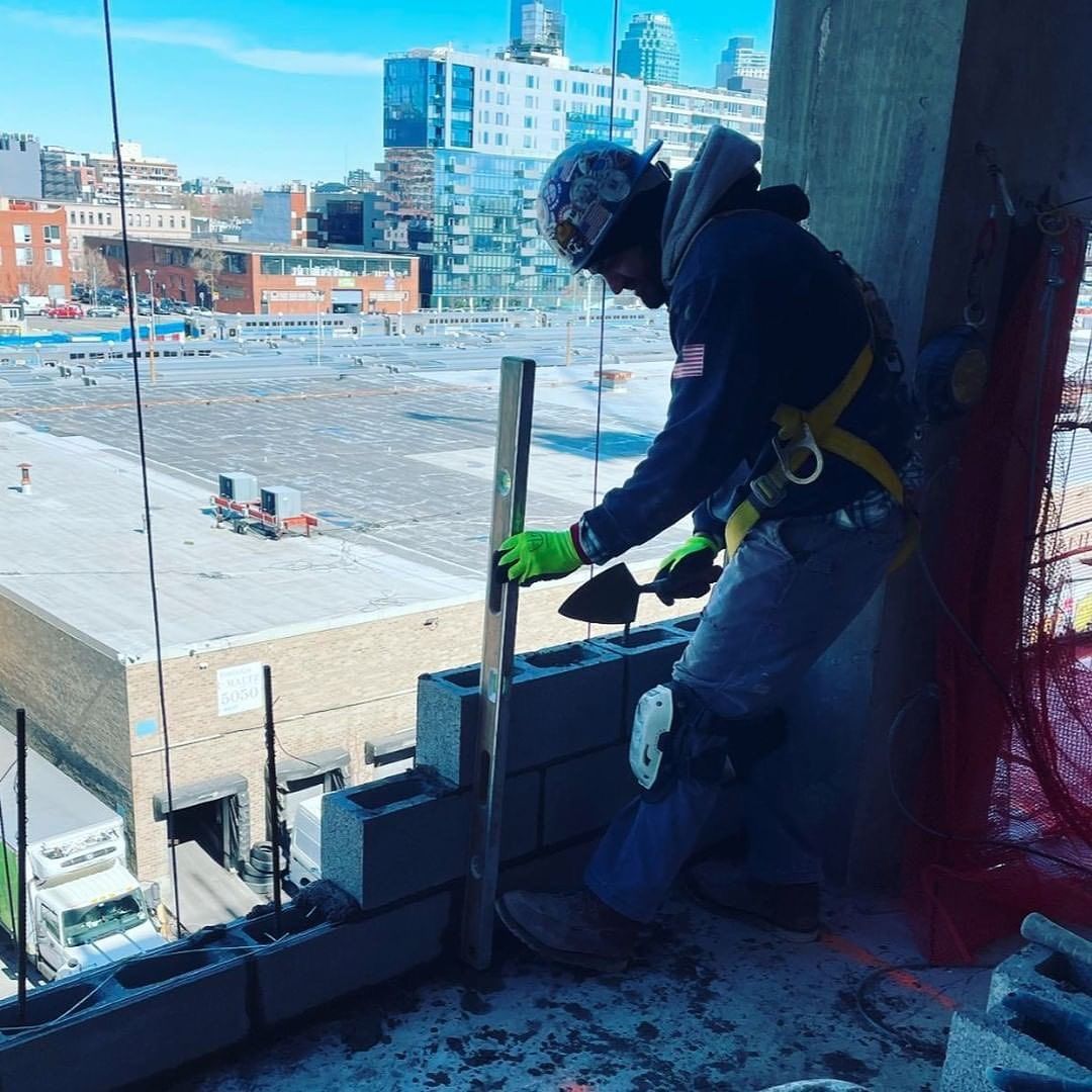 Construction worker in a high-rise building, laying bricks with a trowel. Sunny day, urban setting.