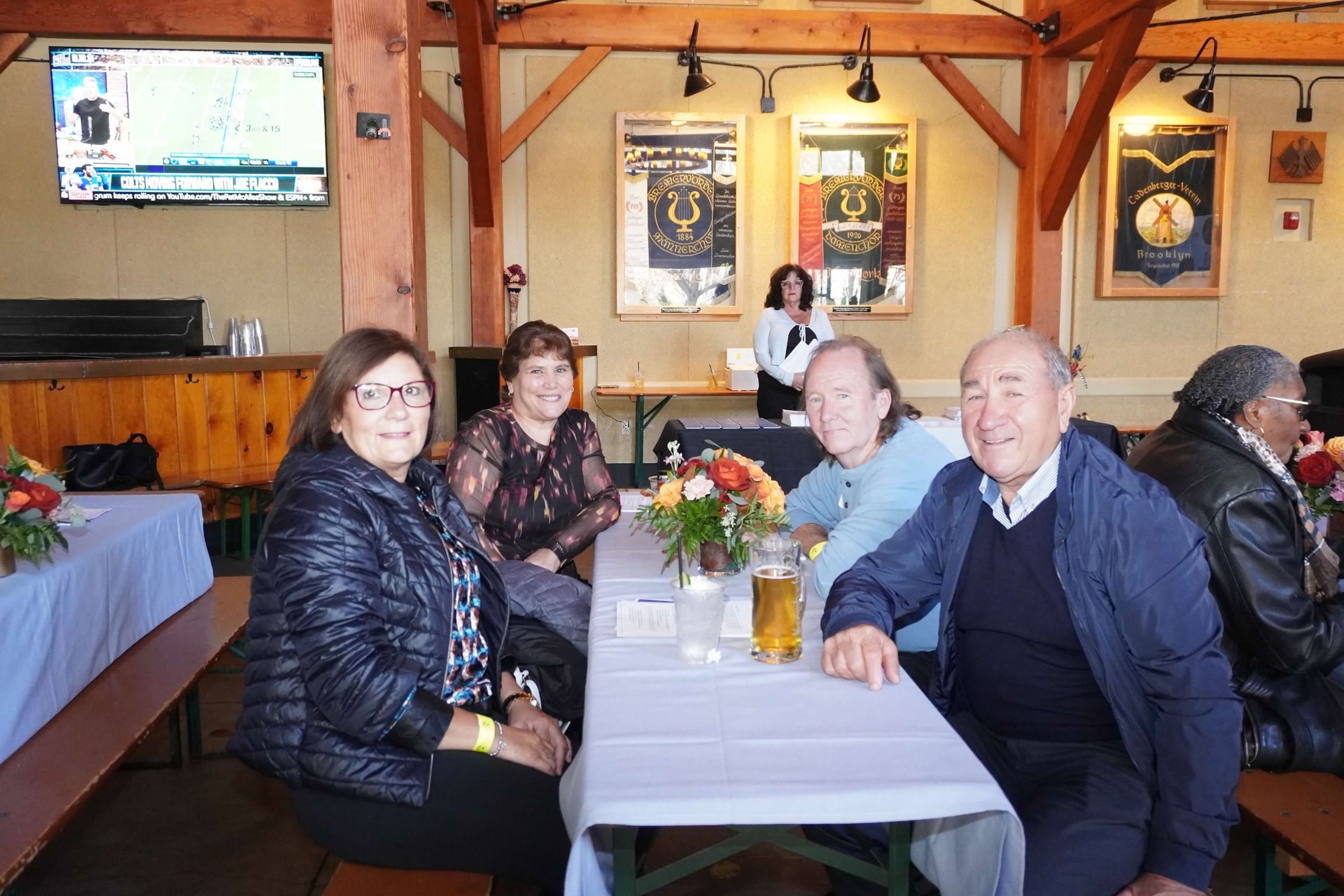 Group of people seated at a table in a restaurant. Some are smiling. Wooden beams and artwork visible.