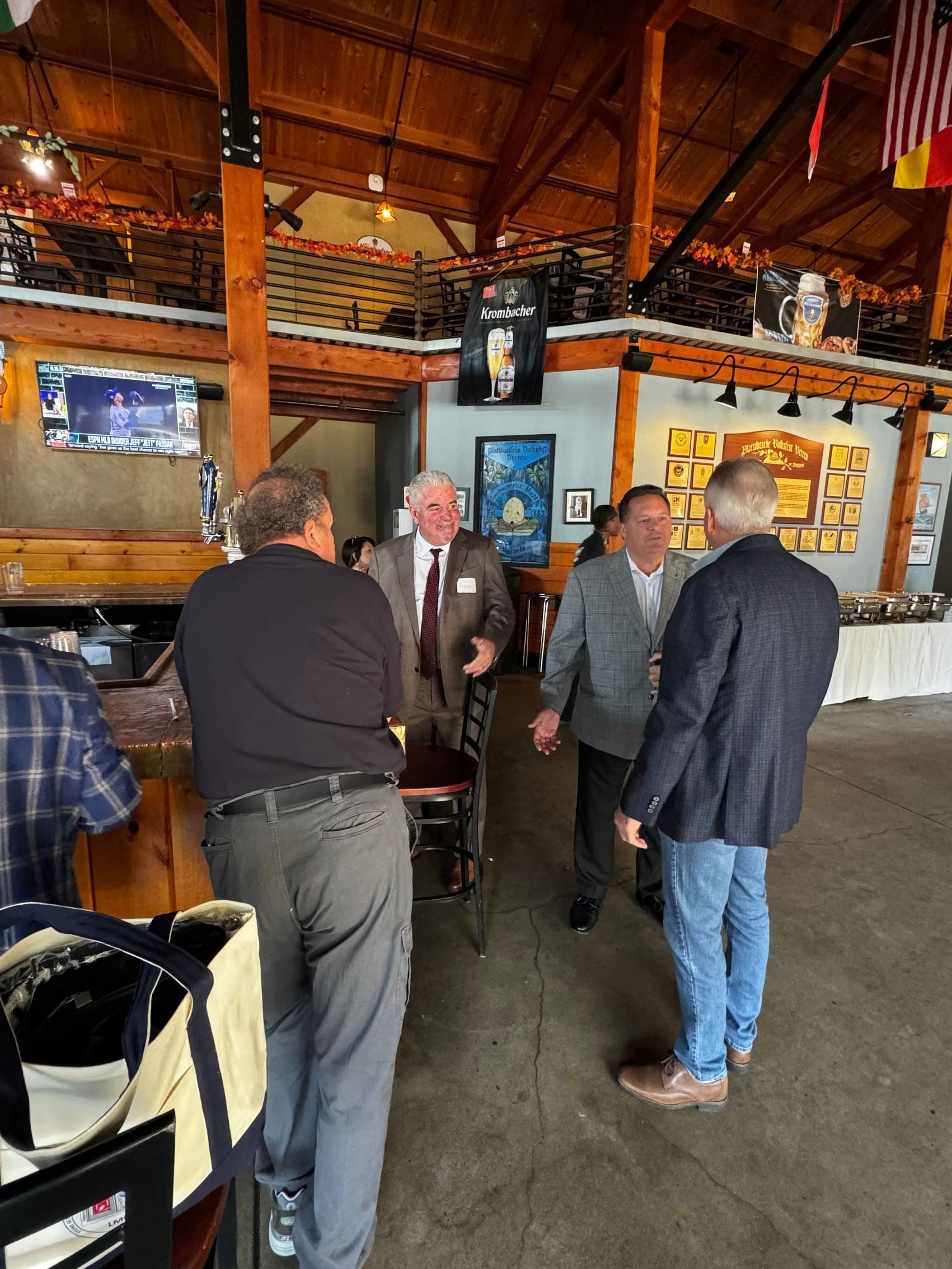 Men in a pub, conversing near a bar.  Wooden interior with flags and decor.