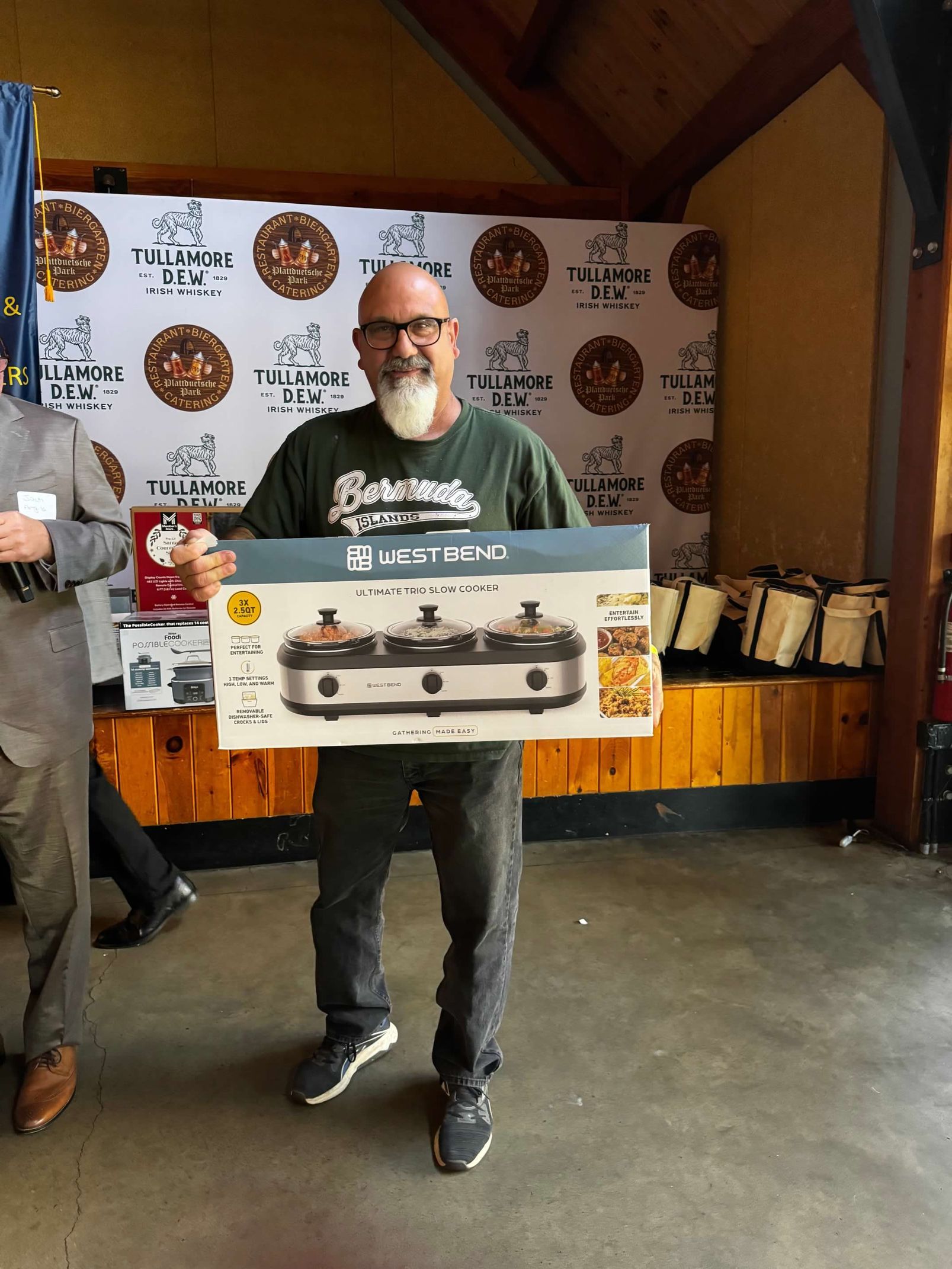 Man holding a box for a three-burner stove, smiling at an event with a backdrop of logos.