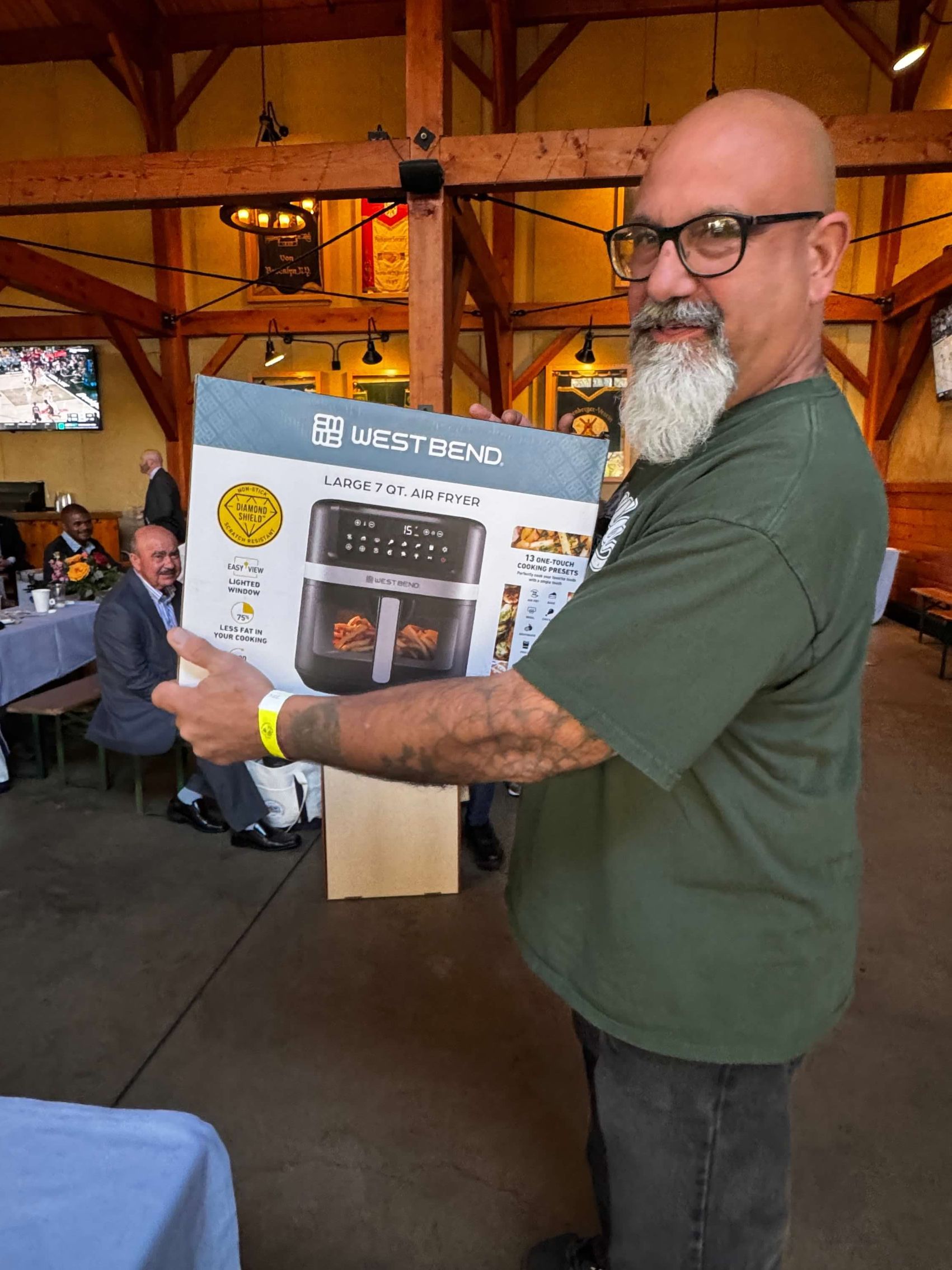 Man with beard holding an air fryer box at a restaurant, smiling.