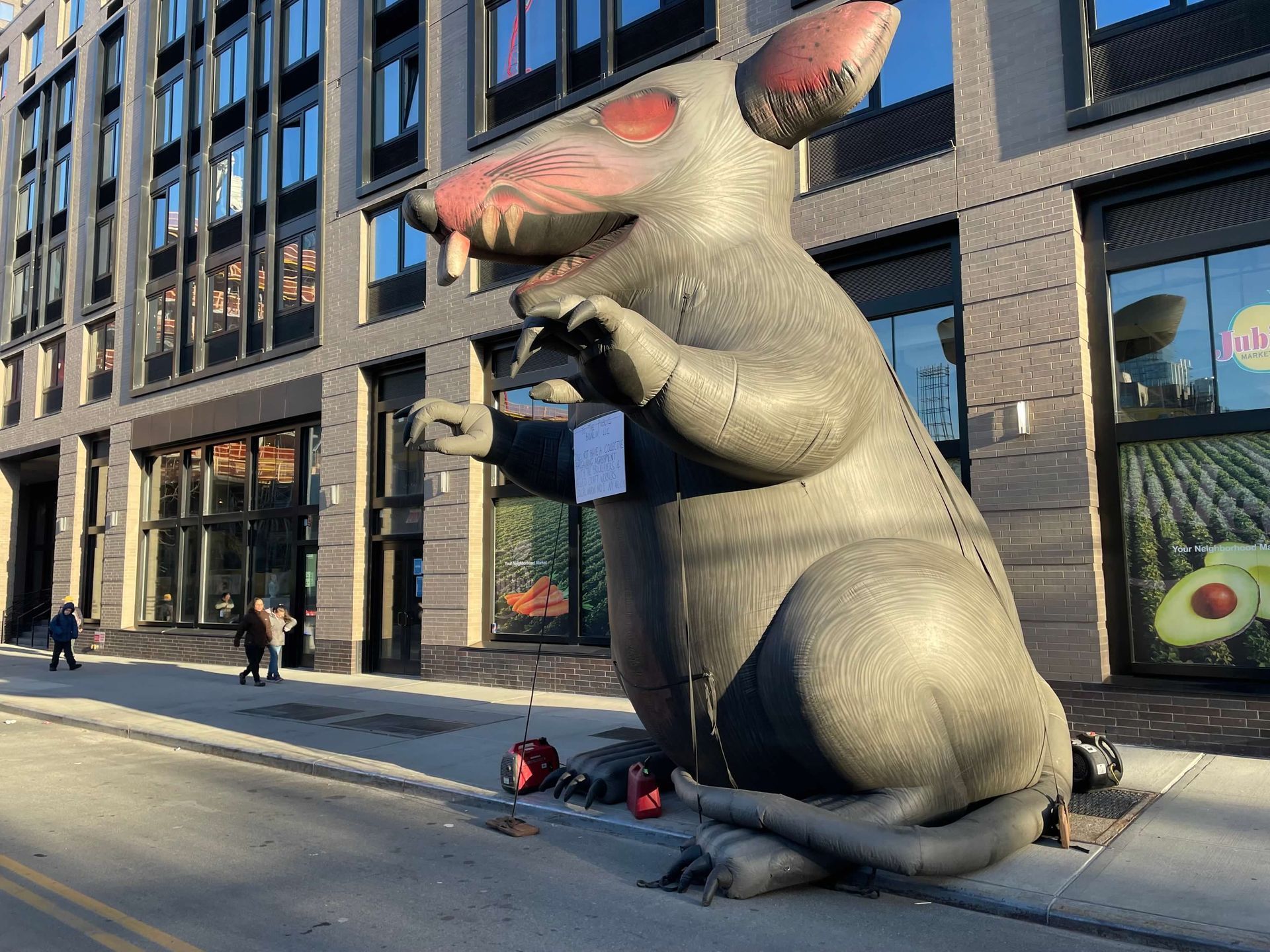 Giant inflatable rat on a city street, gray with red eyes, used as a protest symbol.