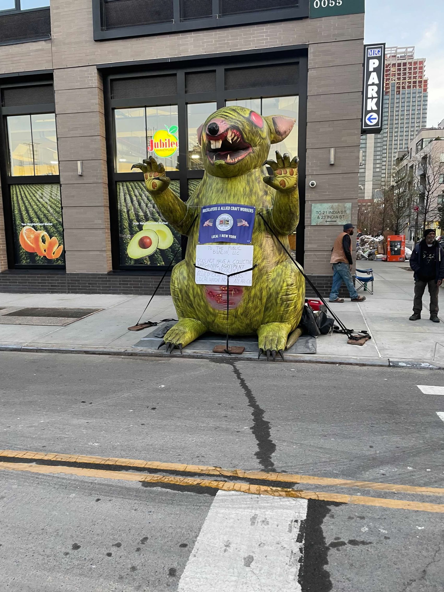 Giant inflatable rat statue on a city street in front of a building.
