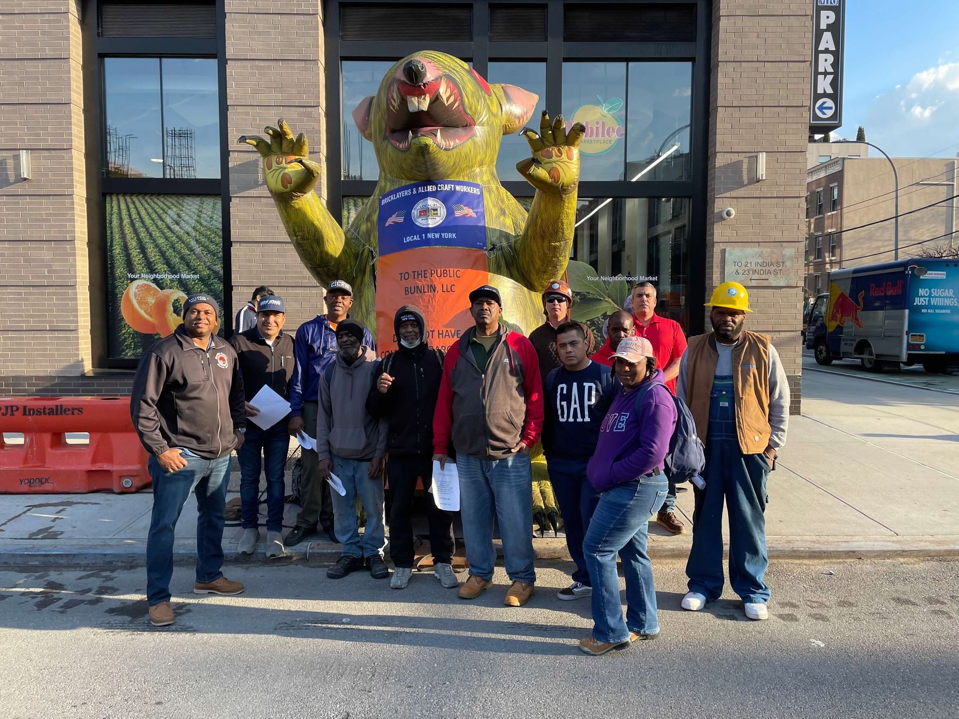 Group of people pose in front of a green rat statue outside a building, some hold papers.