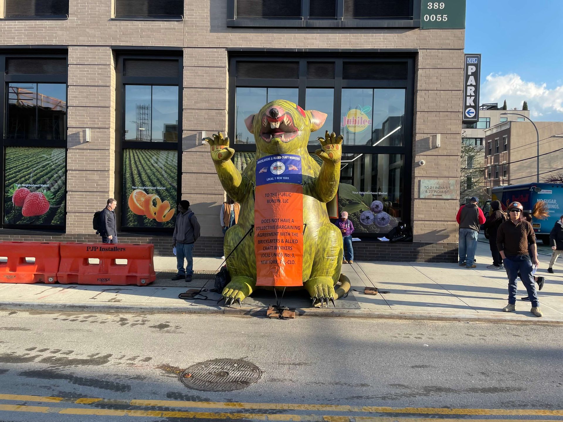 Giant green monster statue in front of a grocery store with people nearby.