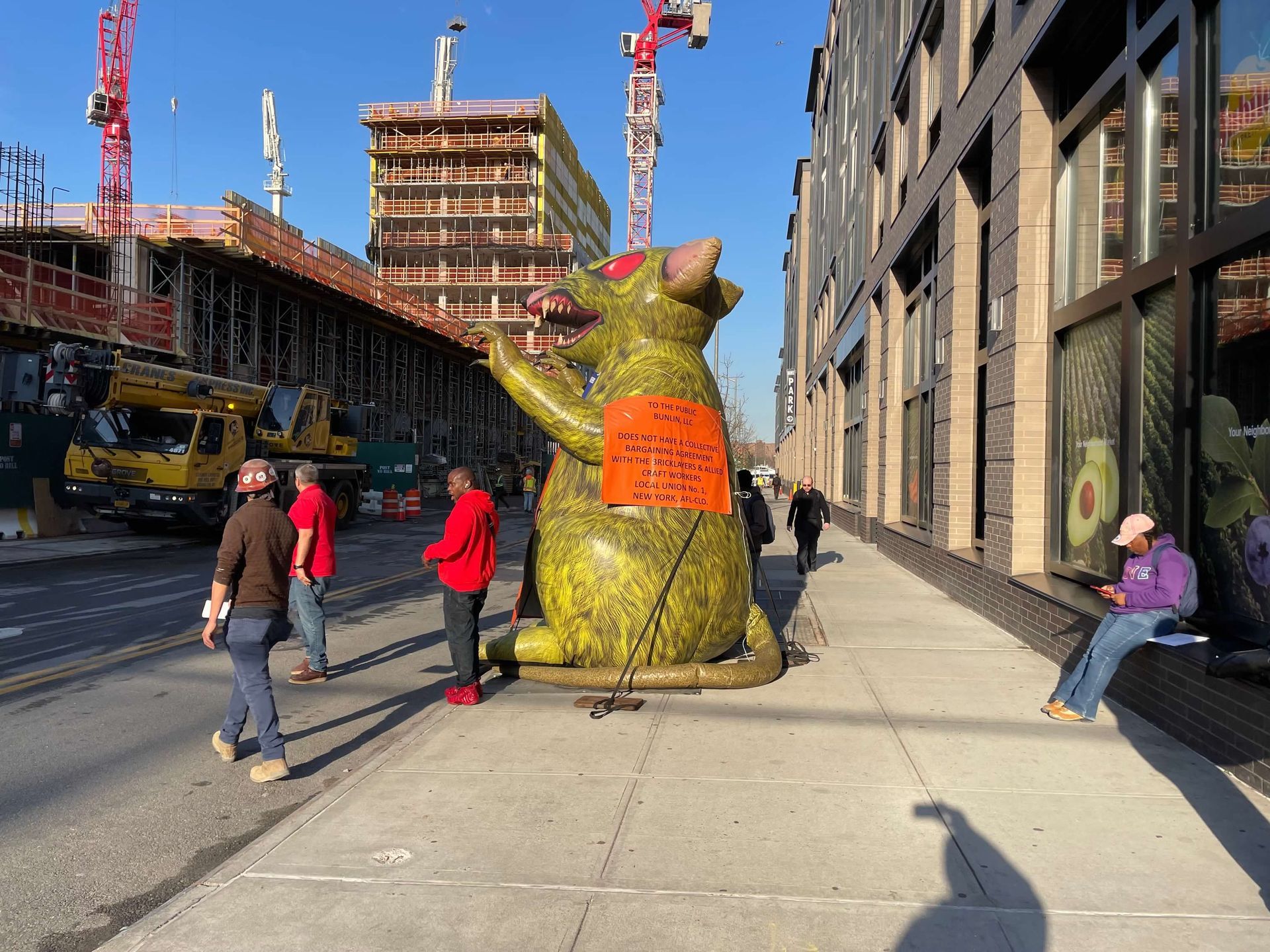 Giant inflatable rat with workers, construction site, street, and building.