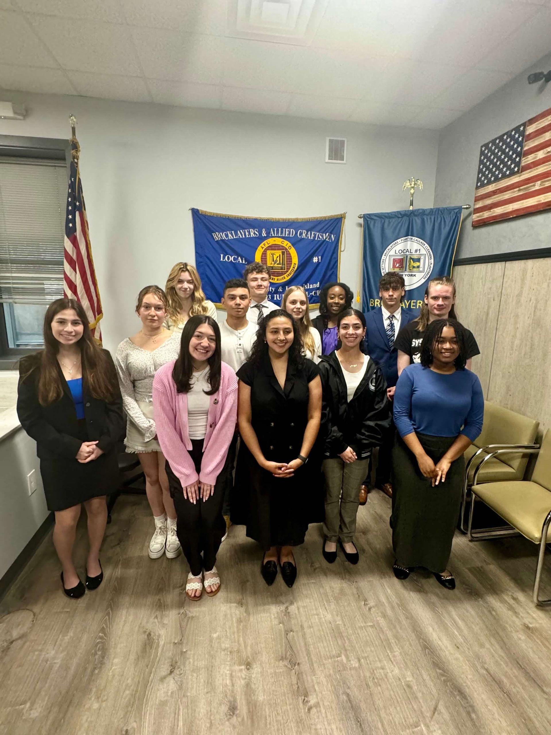 Group of students posing with flags, indoors, smiling.
