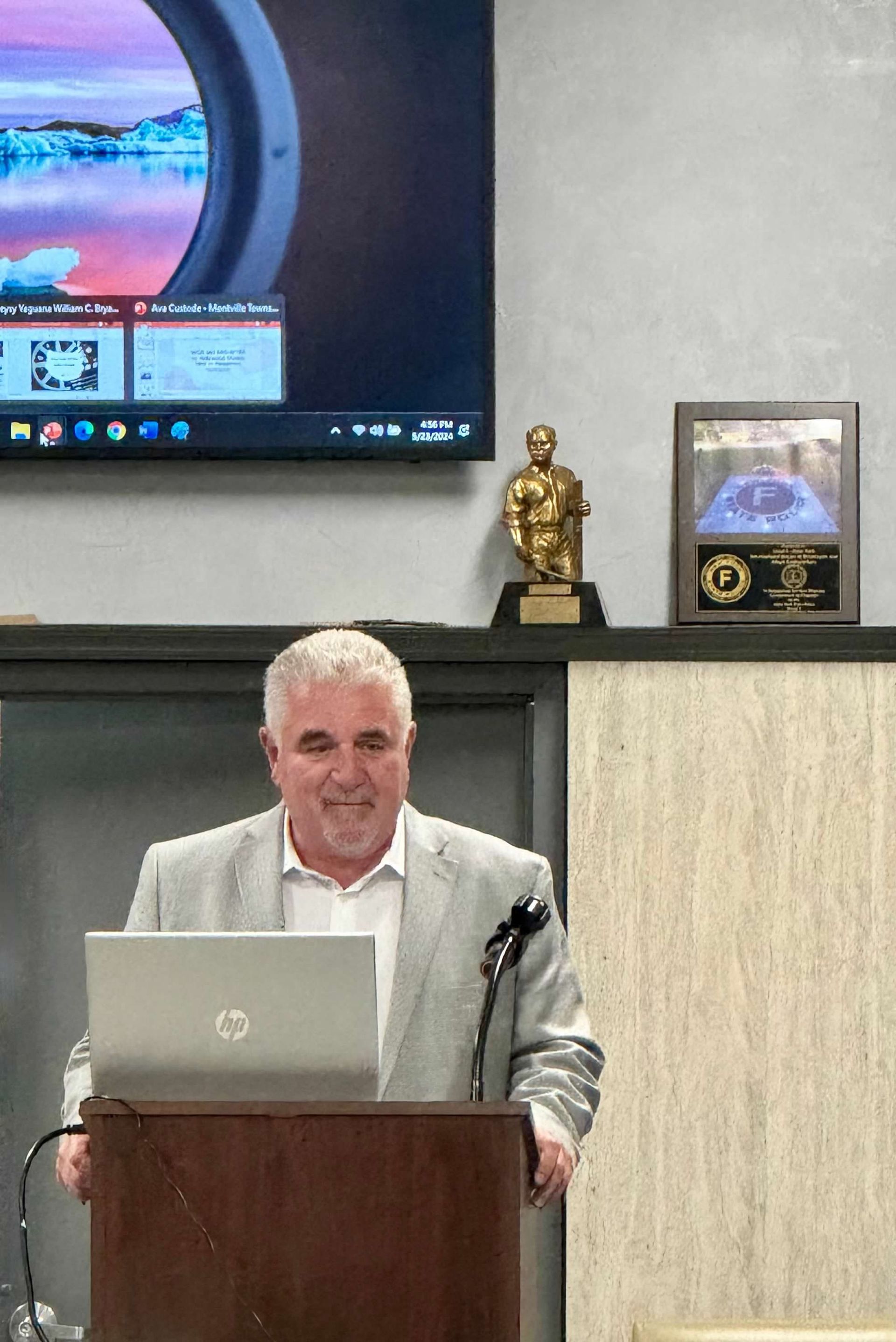 Man in suit, standing at a podium with a laptop, giving a presentation.