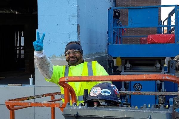 Construction worker in neon vest, giving peace sign from lift.